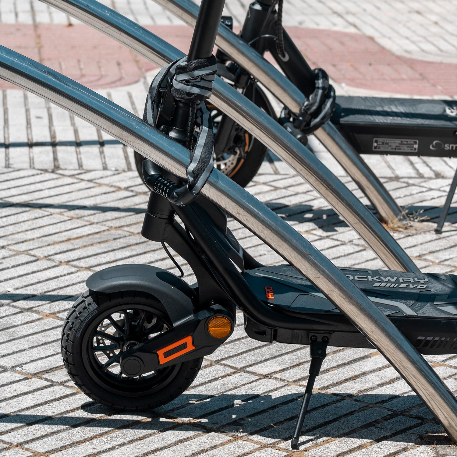 Un scooter negro está asegurado a una barra de metal con un candado de cadena. El candado es negro y plateado.