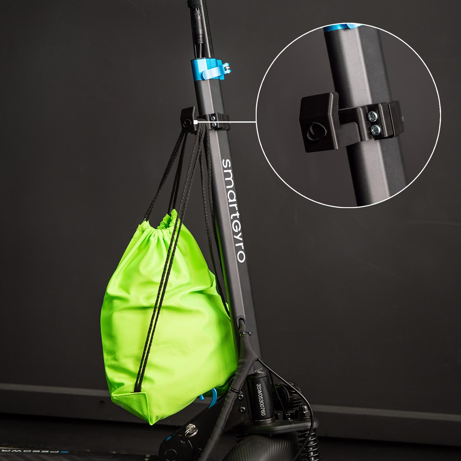 Una bolsa verde con cordón cuelga de un scooter negro. El scooter está sobre un fondo oscuro.