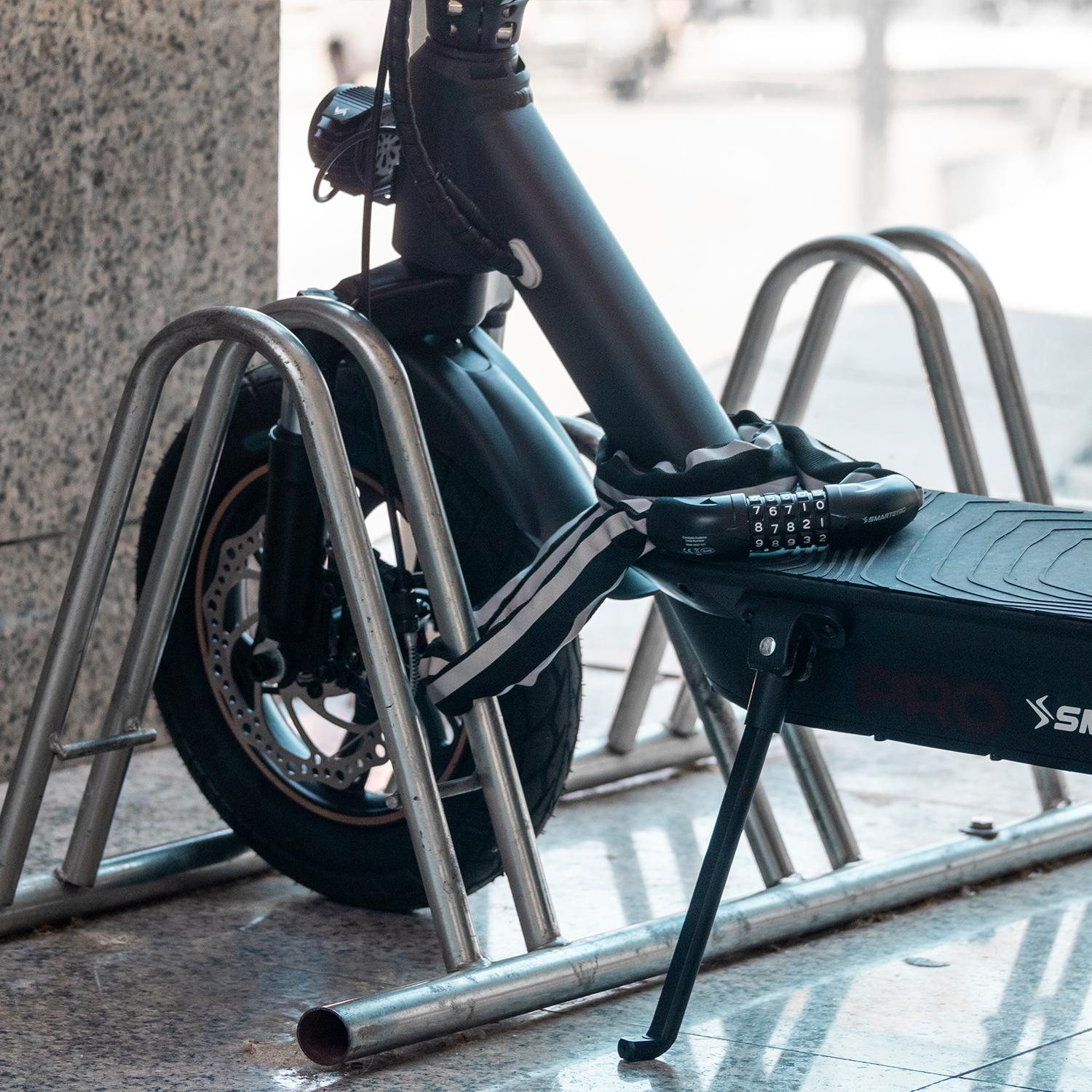 Un scooter está asegurado a una barra de metal con un candado de cadena. El scooter es negro.
