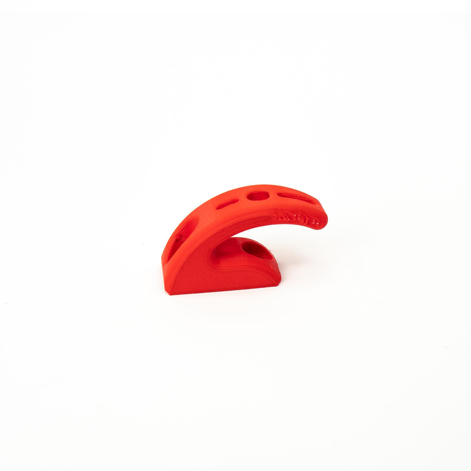 Un objeto de plástico rojo con agujeros sobre fondo blanco. Parece ser un soporte.