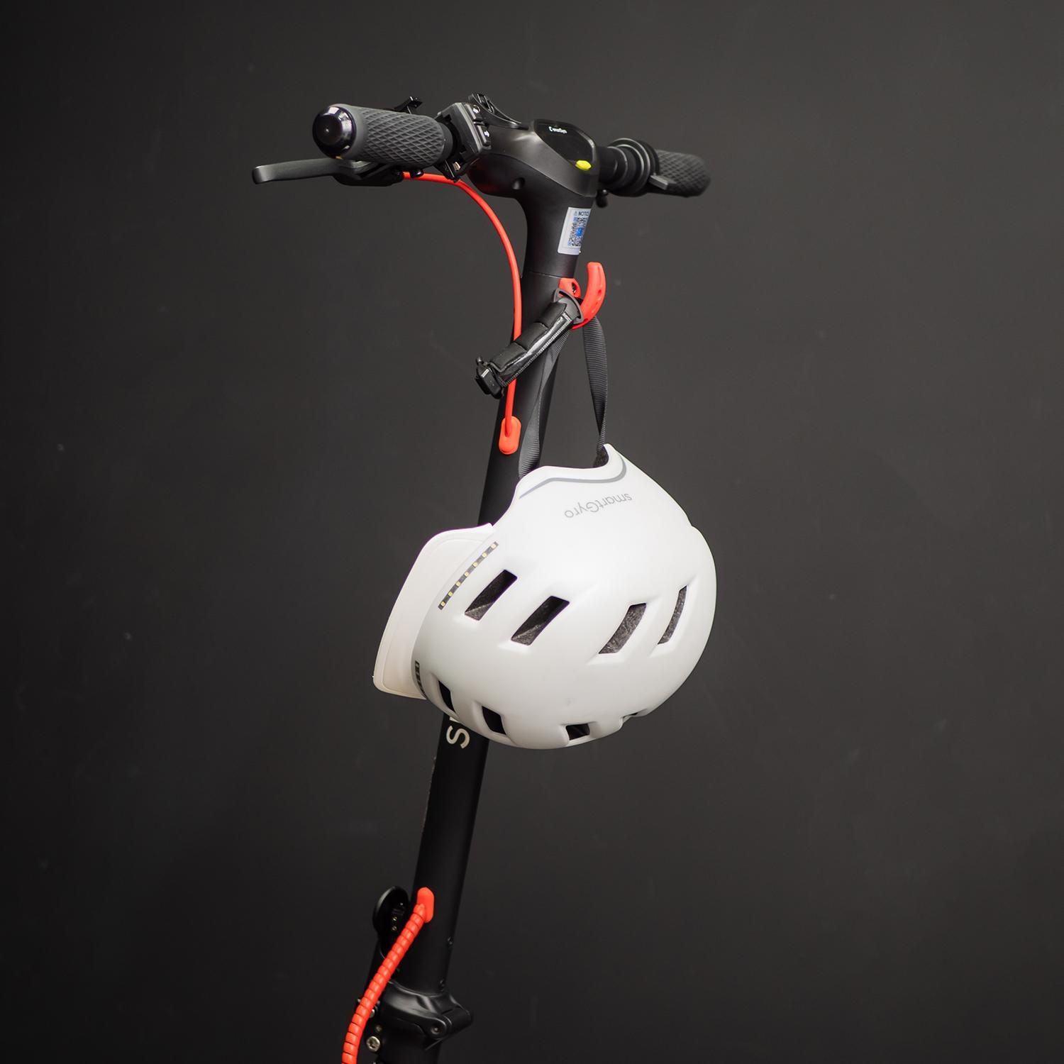 Un casco blanco cuelga de un scooter negro. La escena es contra un fondo oscuro.