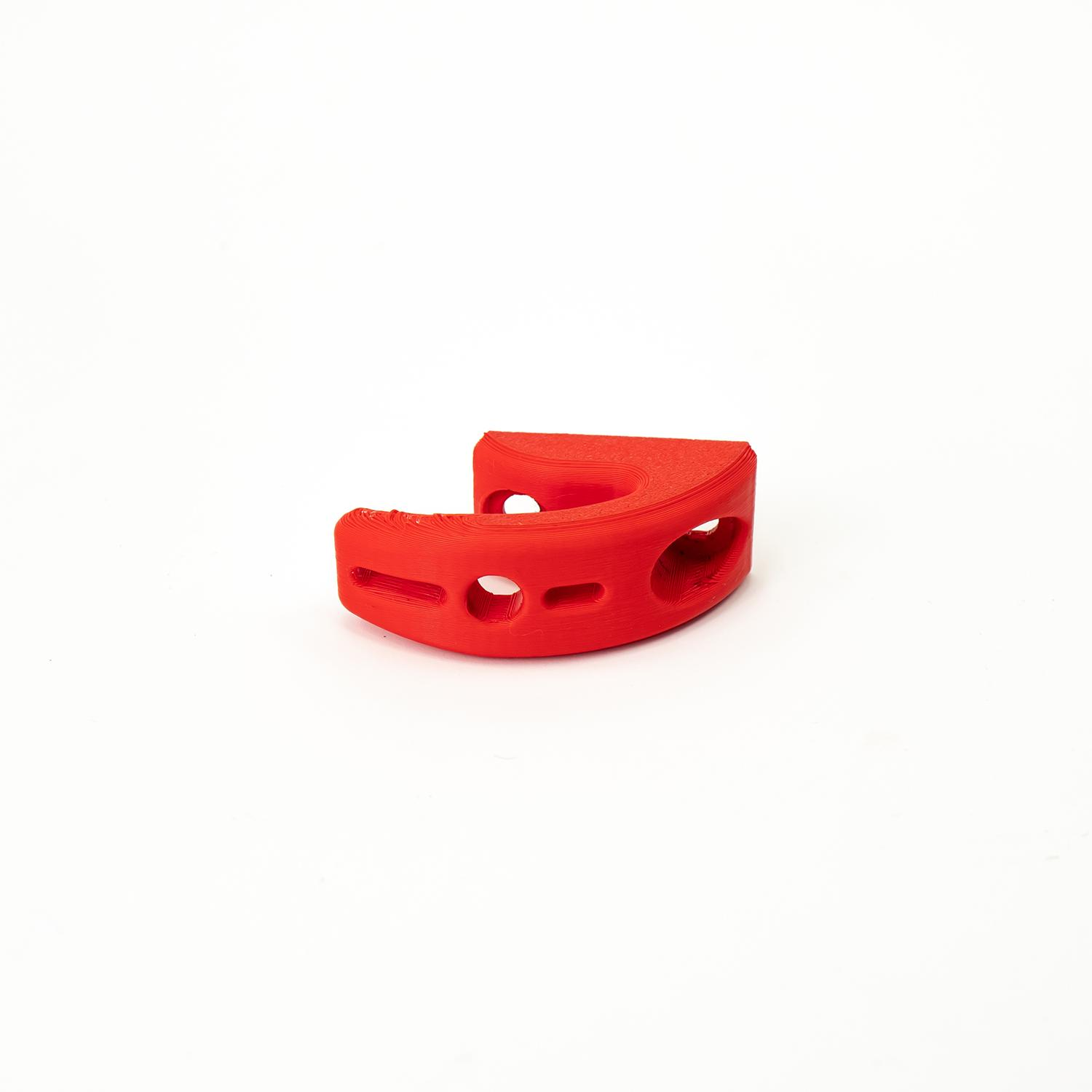 Objeto de plástico rojo con tres agujeros, forma irregular y fondo blanco, probablemente impreso en 3D.