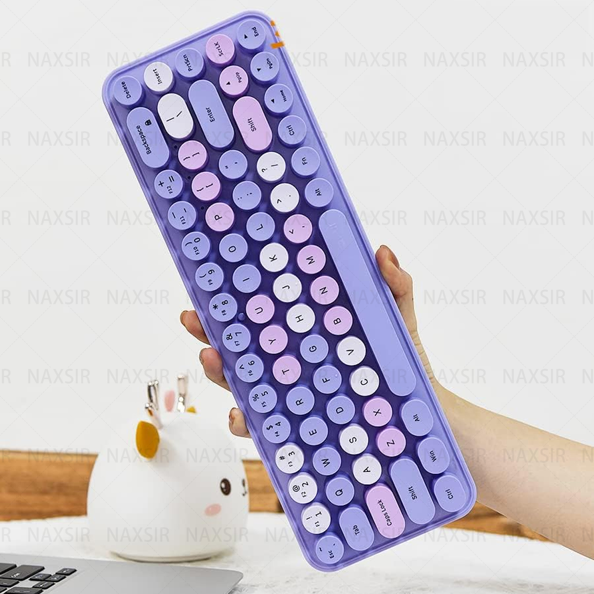 Eine lila Tastatur mit runden Tasten. Eine Hand hält sie. Weißer Hintergrund.