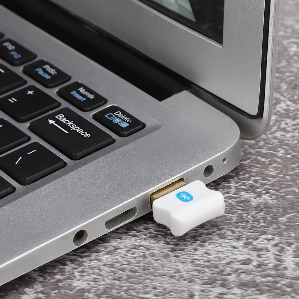 Ein weißer Bluetooth-Adapter ist an einen USB-Anschluss eines Laptops angeschlossen. Der Adapter hat ein Bluetooth-Symbol.