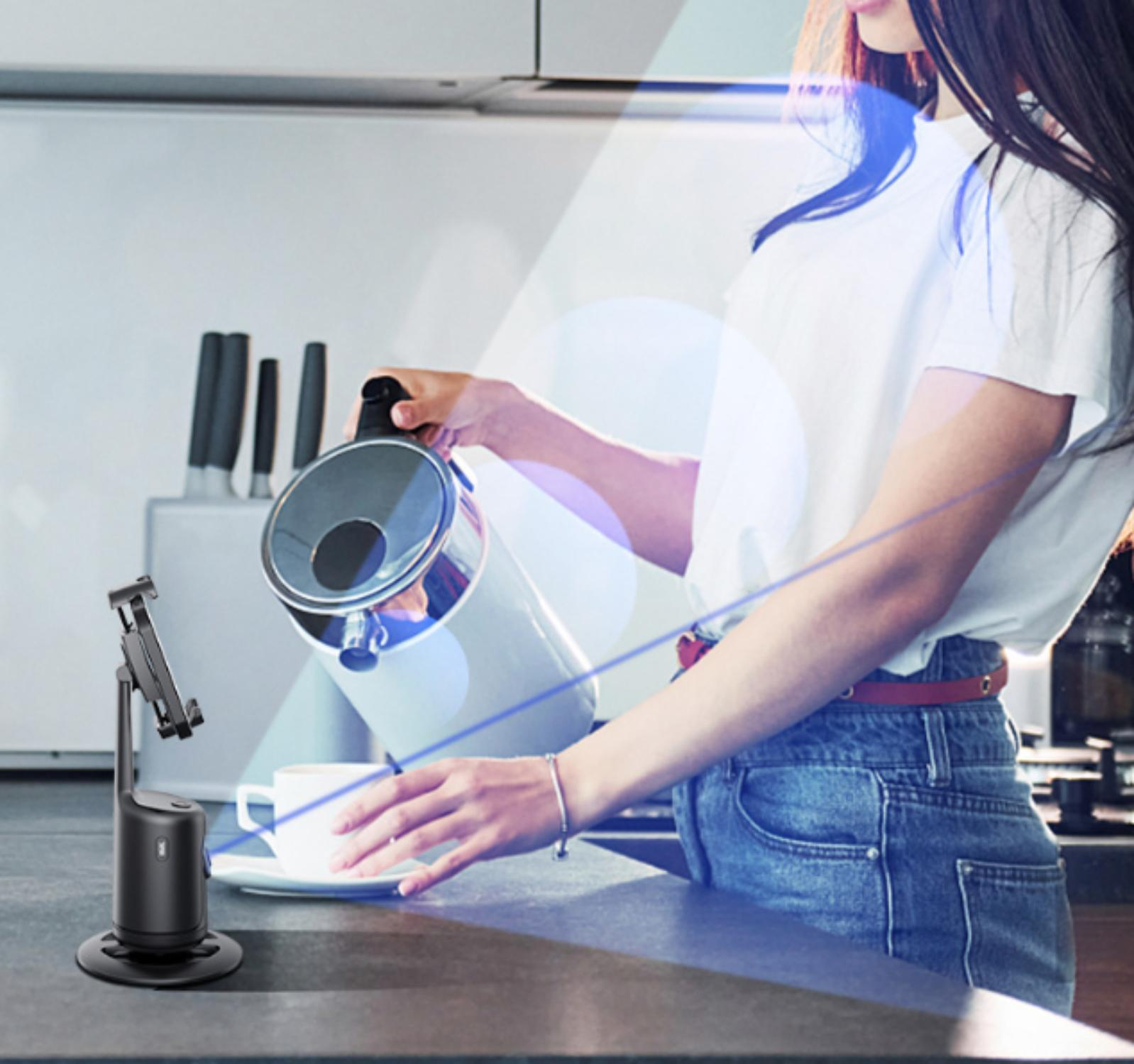 Eine Frau gießt Wasser aus einem Wasserkocher in eine Tasse, mit einem Telefonhalter links im Bild.