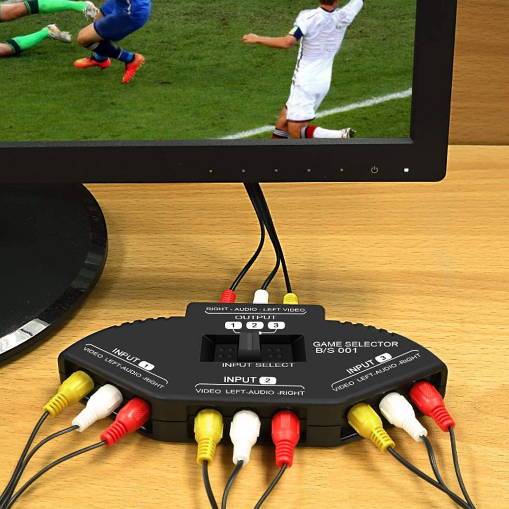 Spielauswähler, der mit RCA-Kabeln an einen Monitor angeschlossen ist, mit einem Fußballspiel auf dem Bildschirm. Holztisch.