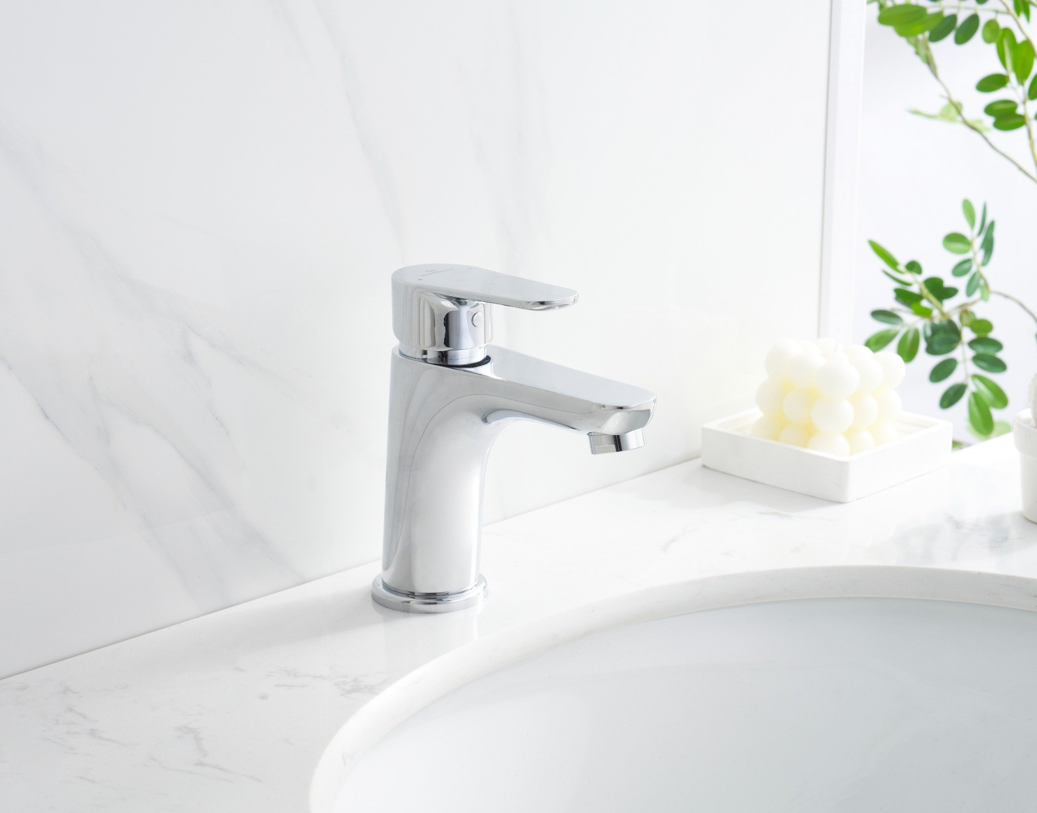Chrom-Wasserhahn auf weißer Arbeitsplatte im Badezimmer. Ein weißes Waschbecken ist sichtbar. Marmorhintergrund.