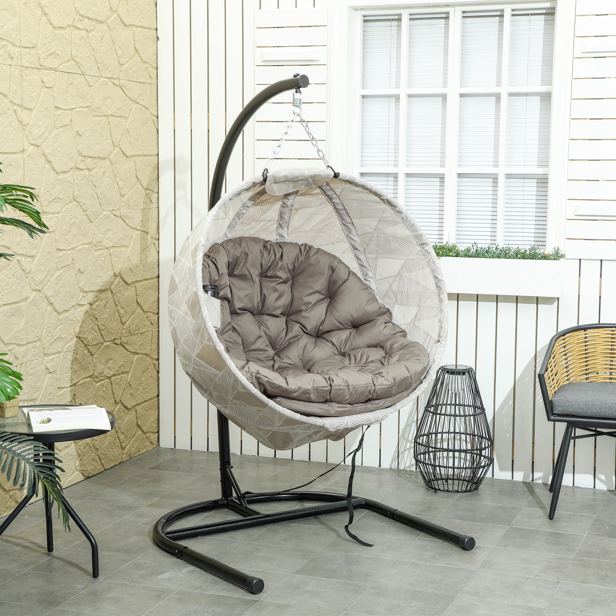 Hänge-Ei-Stuhl mit grauem Kissen. Im Hintergrund Terrasse mit Fenster und Stuhl.
