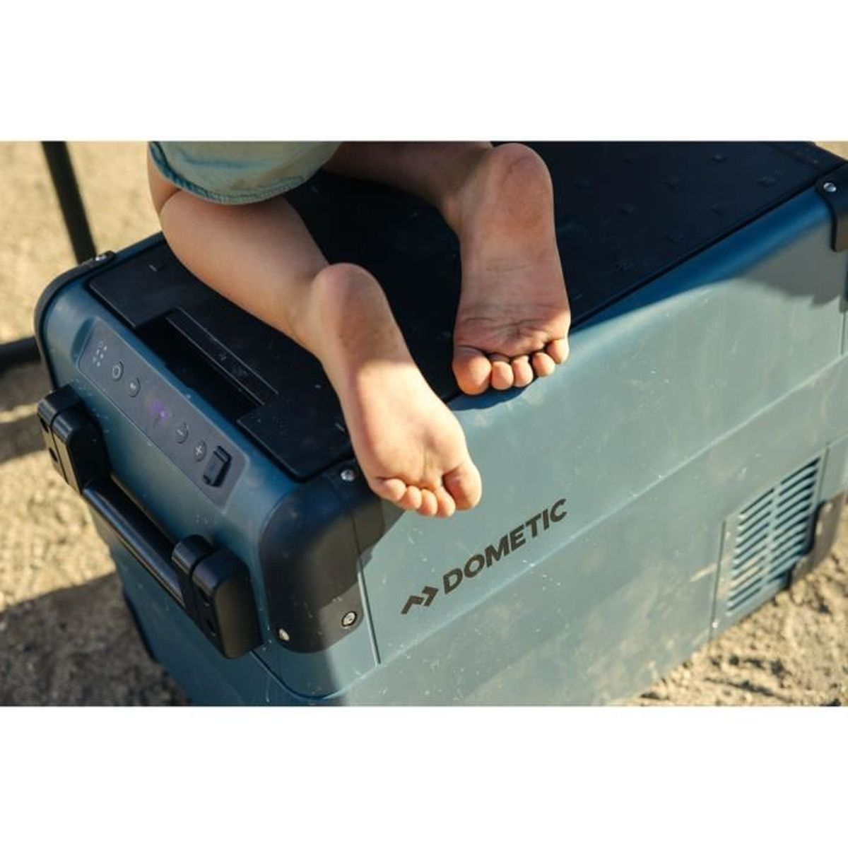 Piedi di un bambino su un refrigeratore verde acqua. Sul refrigeratore c'è la scritta Dometic.