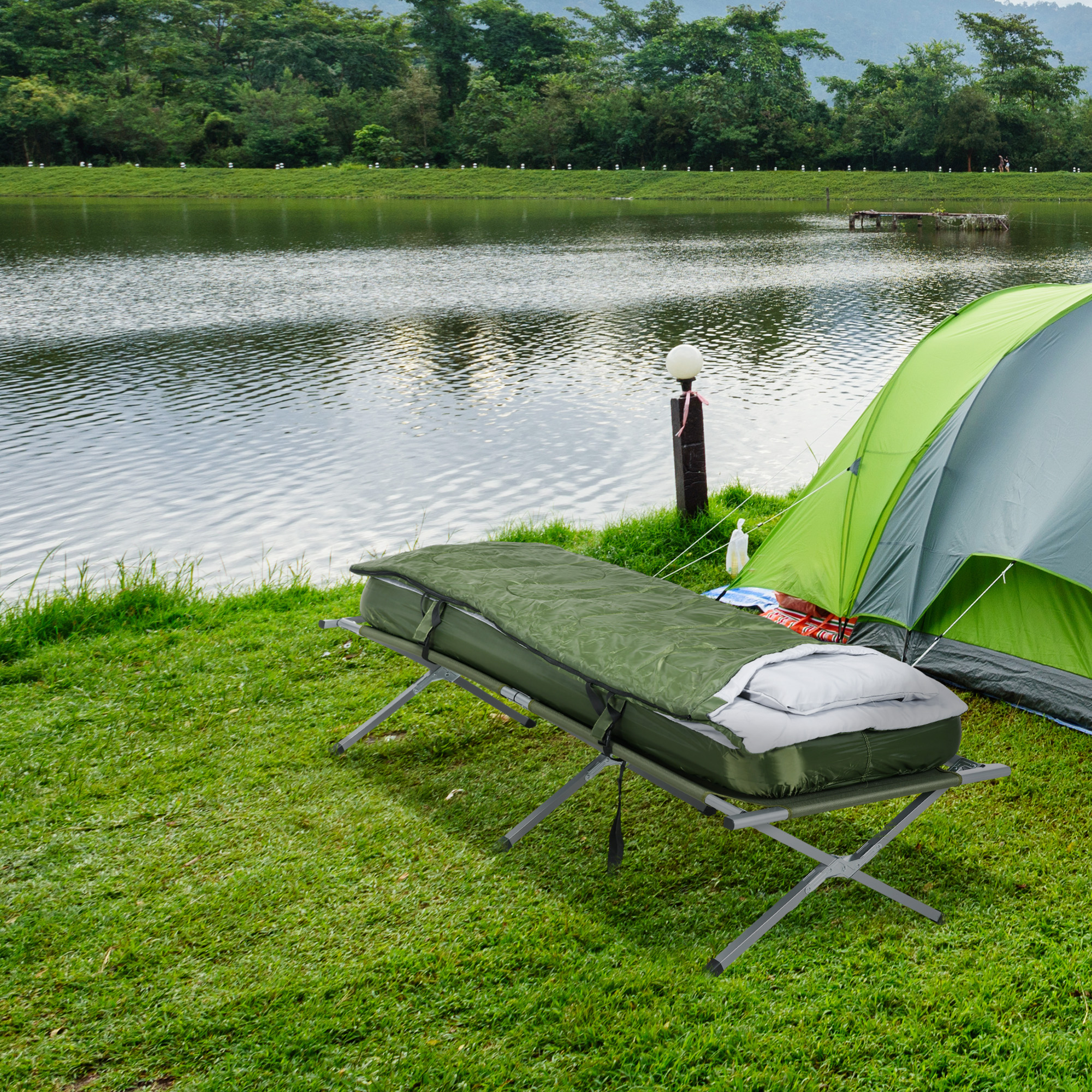 Eine Campingszene mit Feldbett und Zelt in der Nähe eines Sees. Grünes Gras umgibt die Szene.