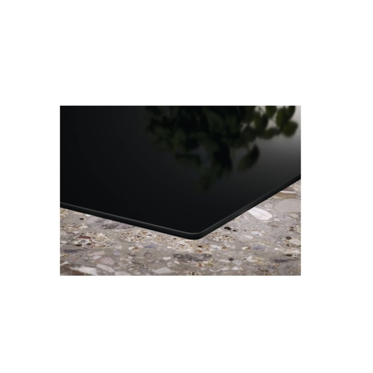 Primo piano di un piano cottura in ceramica nera su un piano di lavoro grigio screziato, con foglie riflesse.