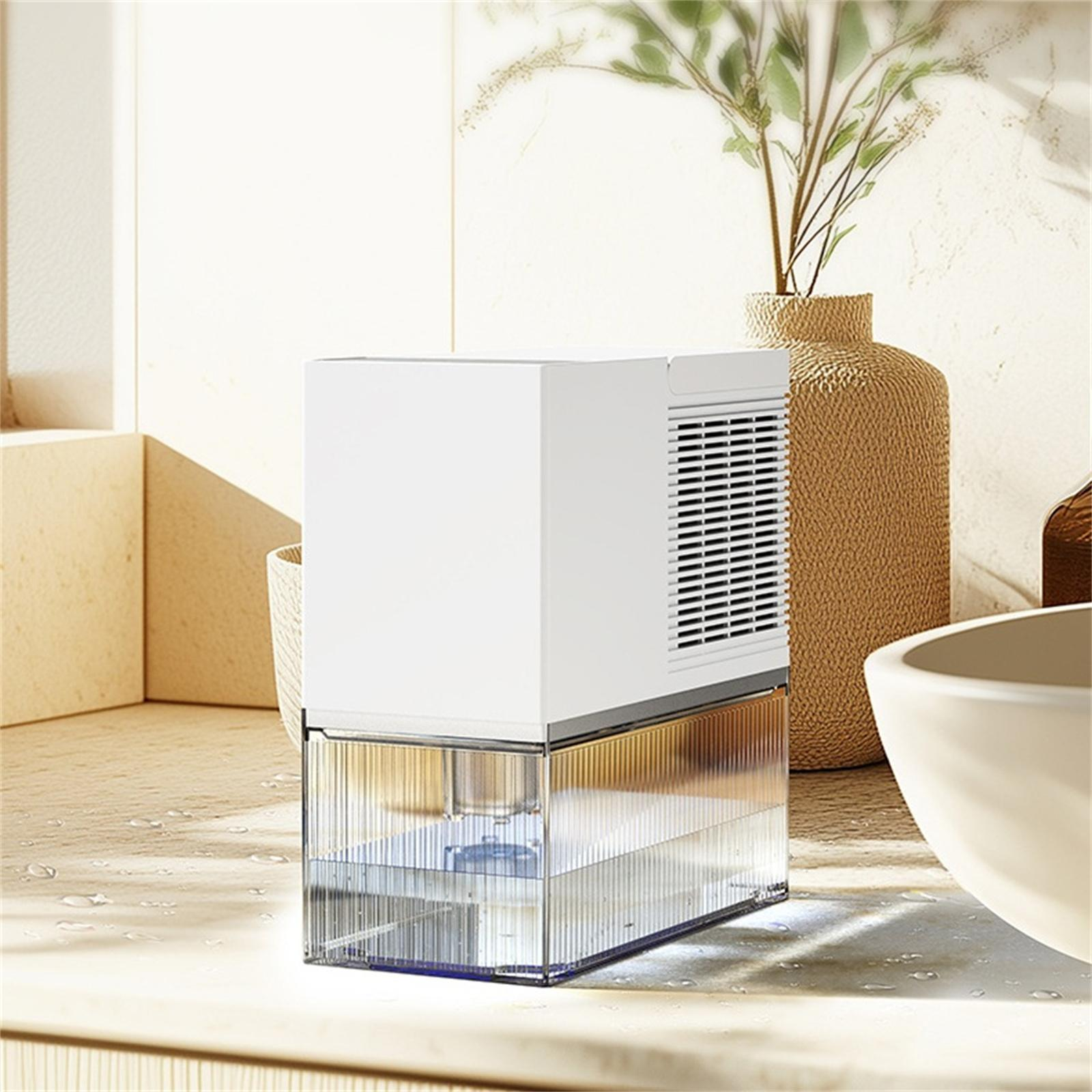 Ein weißer Luftentfeuchter mit einem transparenten Wassertank steht auf einer Oberfläche. Im Hintergrund eine Vase mit Pflanzen.