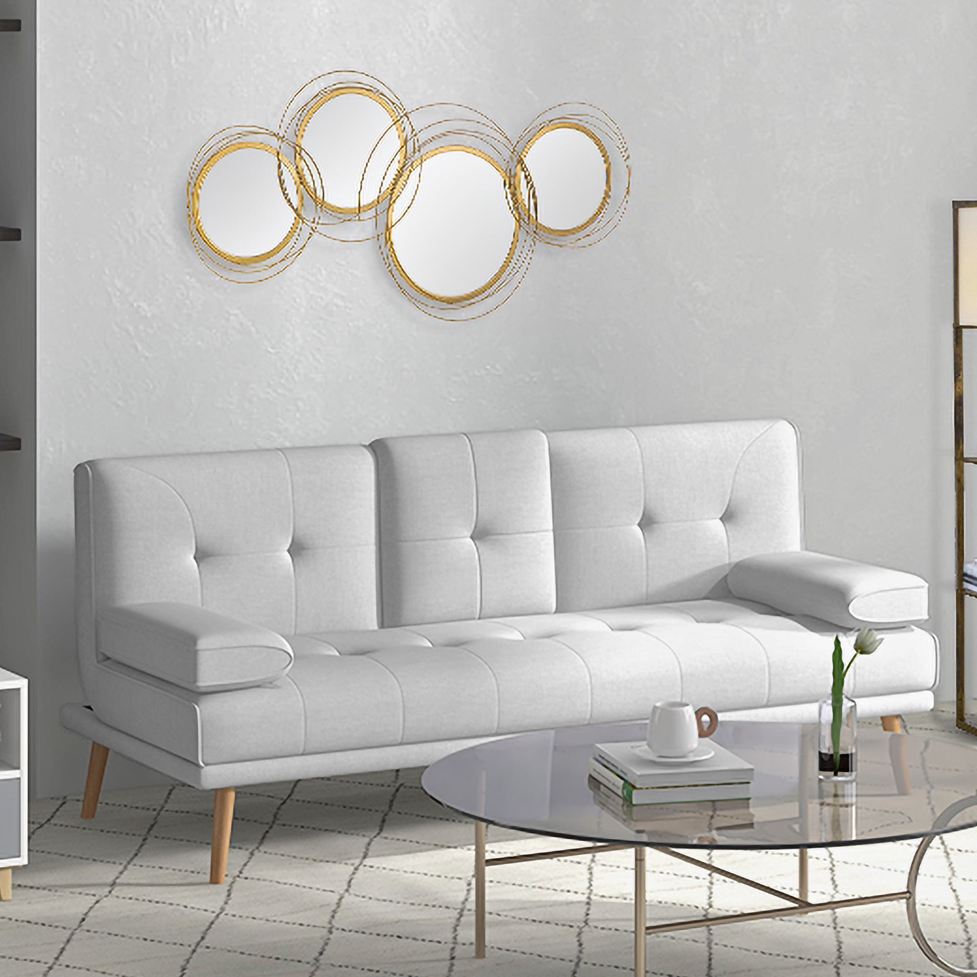 Ein weißes Sofa, ein Glastisch mit einer Tasse und einer Vase und ein goldener Kreisspiegel an der Wand.