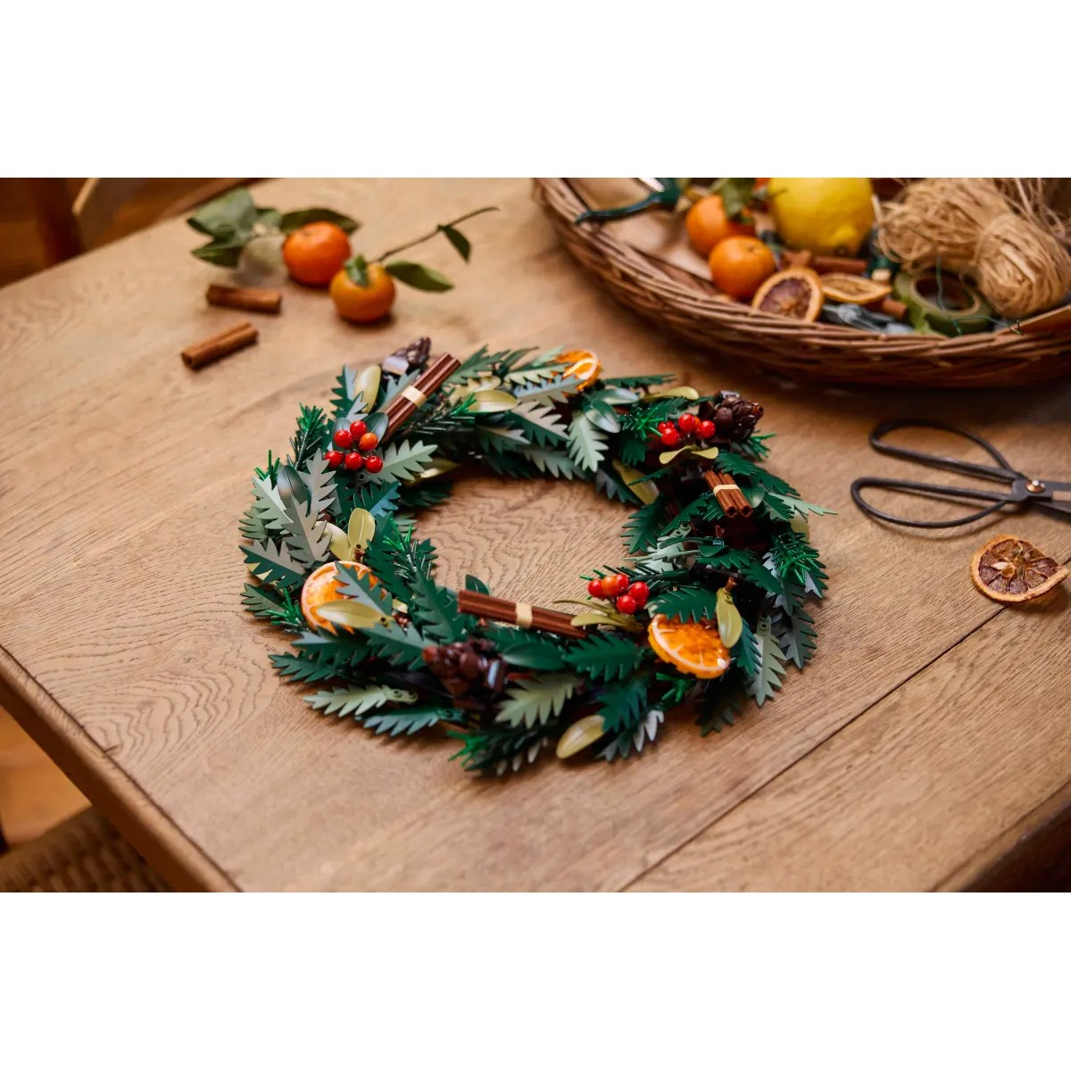 Een kerstkrans met dennenappels, sinaasappels, kaneelstokjes en rode bessen op een houten tafel.