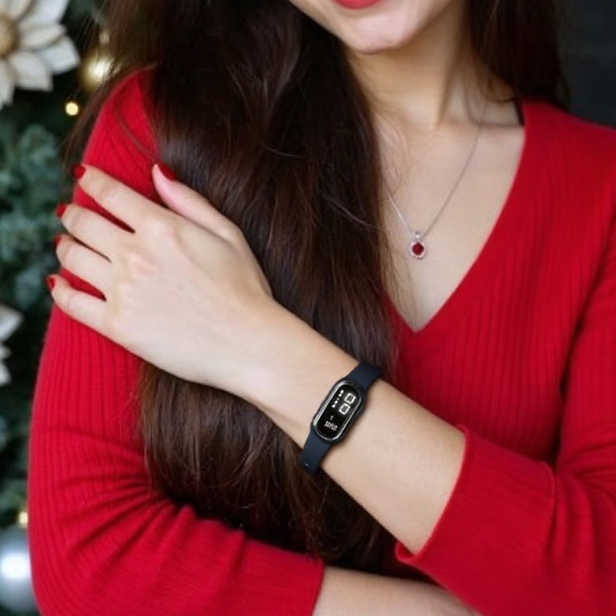 Frau trägt einen roten Pullover, mit einer schwarzen Smartwatch am Handgelenk. Die Uhr zeigt Zeit und Metriken an.