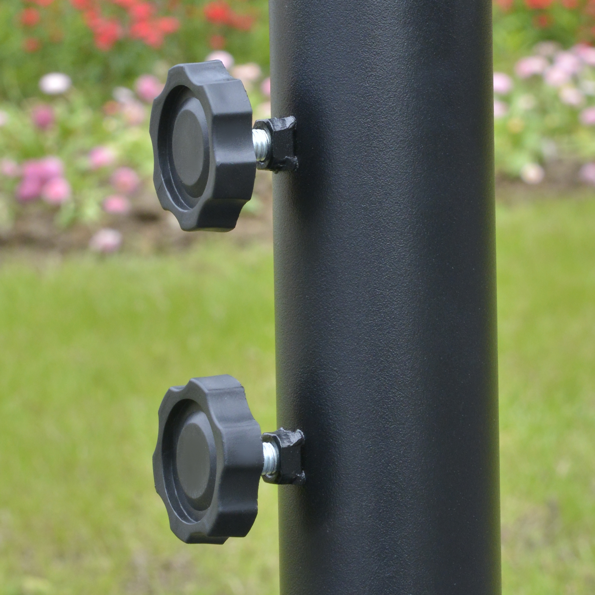 Eine schwarze Metallstange mit zwei schwarzen Knöpfen, vermutlich Teil eines Gartenschirms.