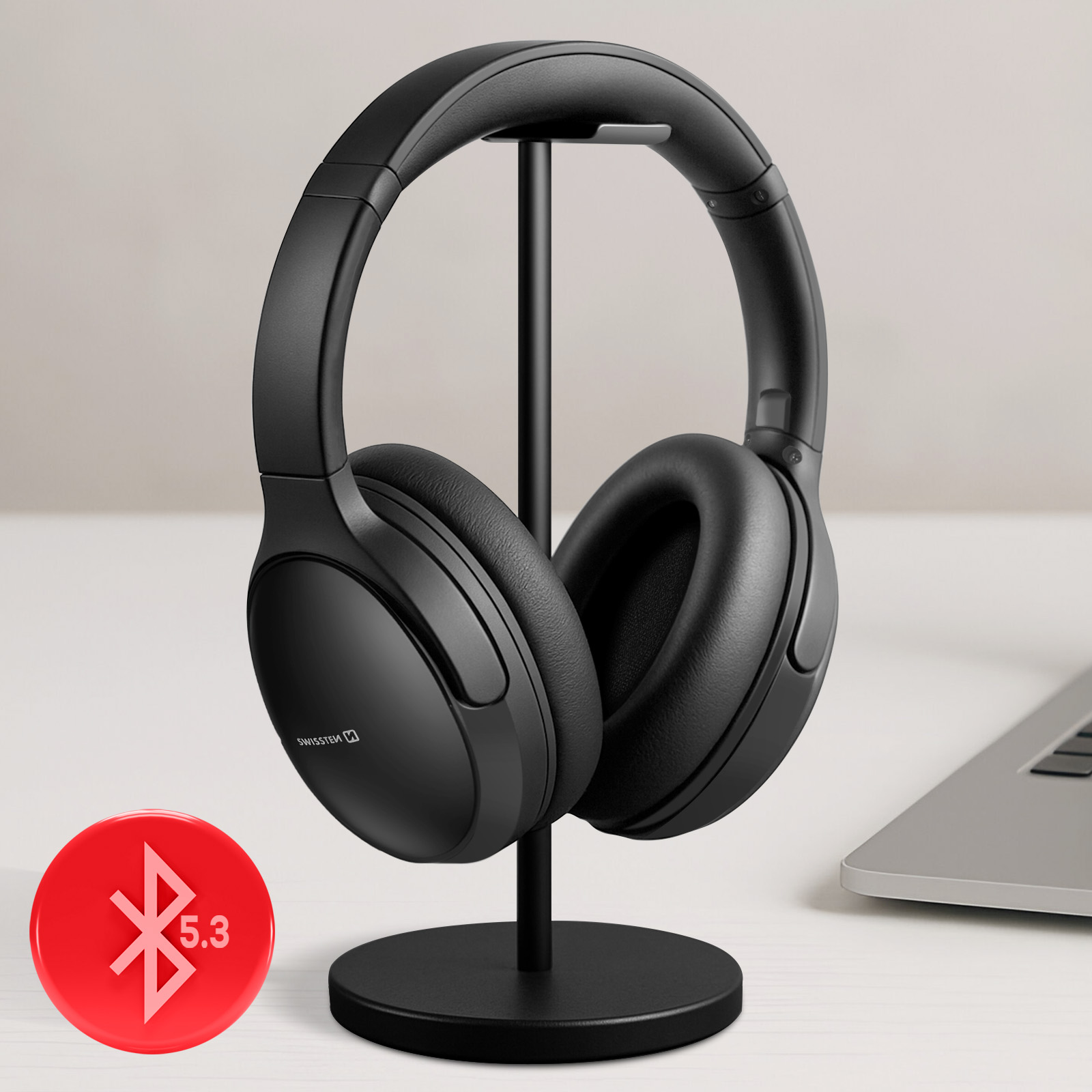 Schwarze Kopfhörer auf einem Ständer mit Bluetooth-Symbol und Laptop im Hintergrund.