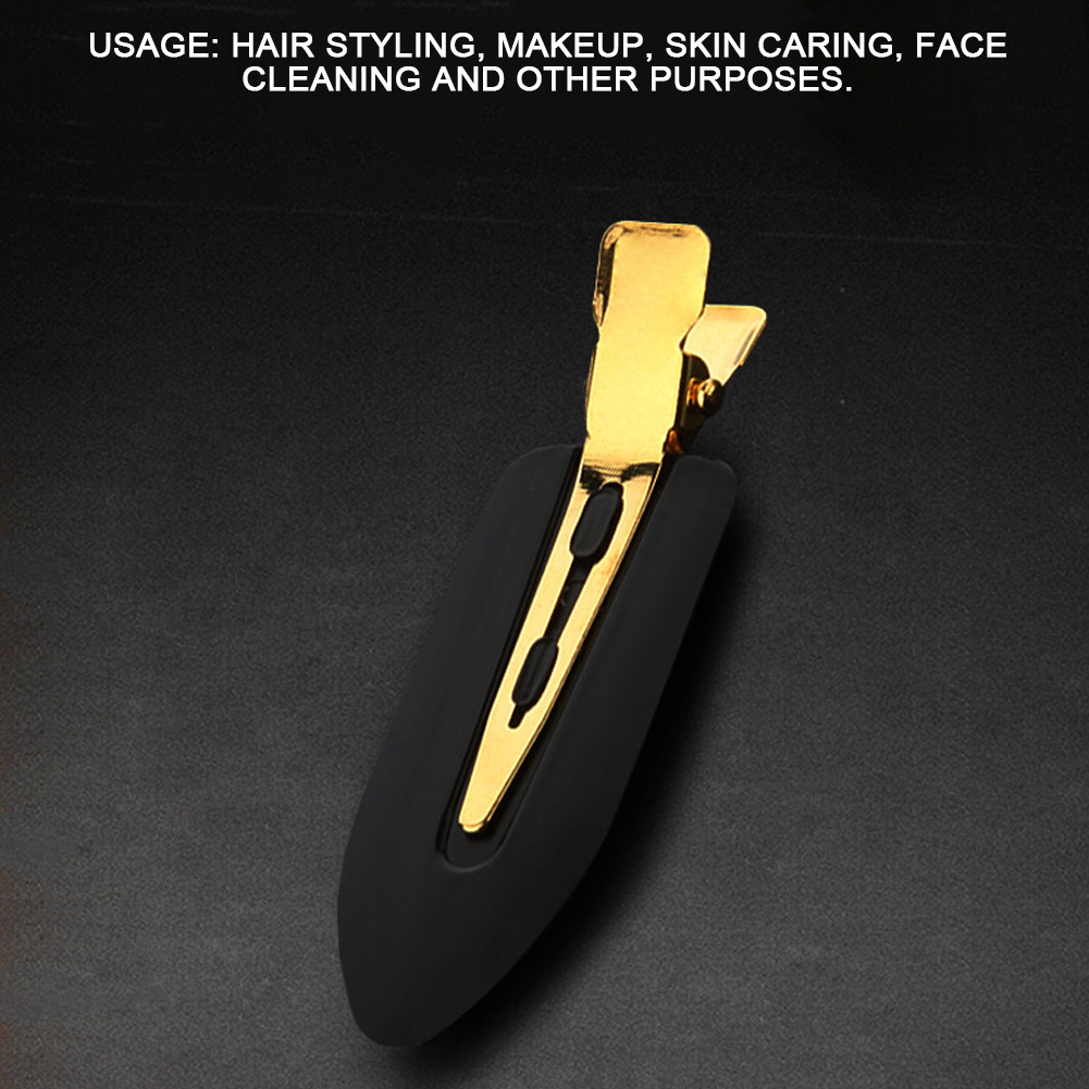Eine einzelne schwarze Haarspange mit Goldmetall. Die Spange ist wie ein abgeflachter Tropfen geformt. Schwarzer Hintergrund.