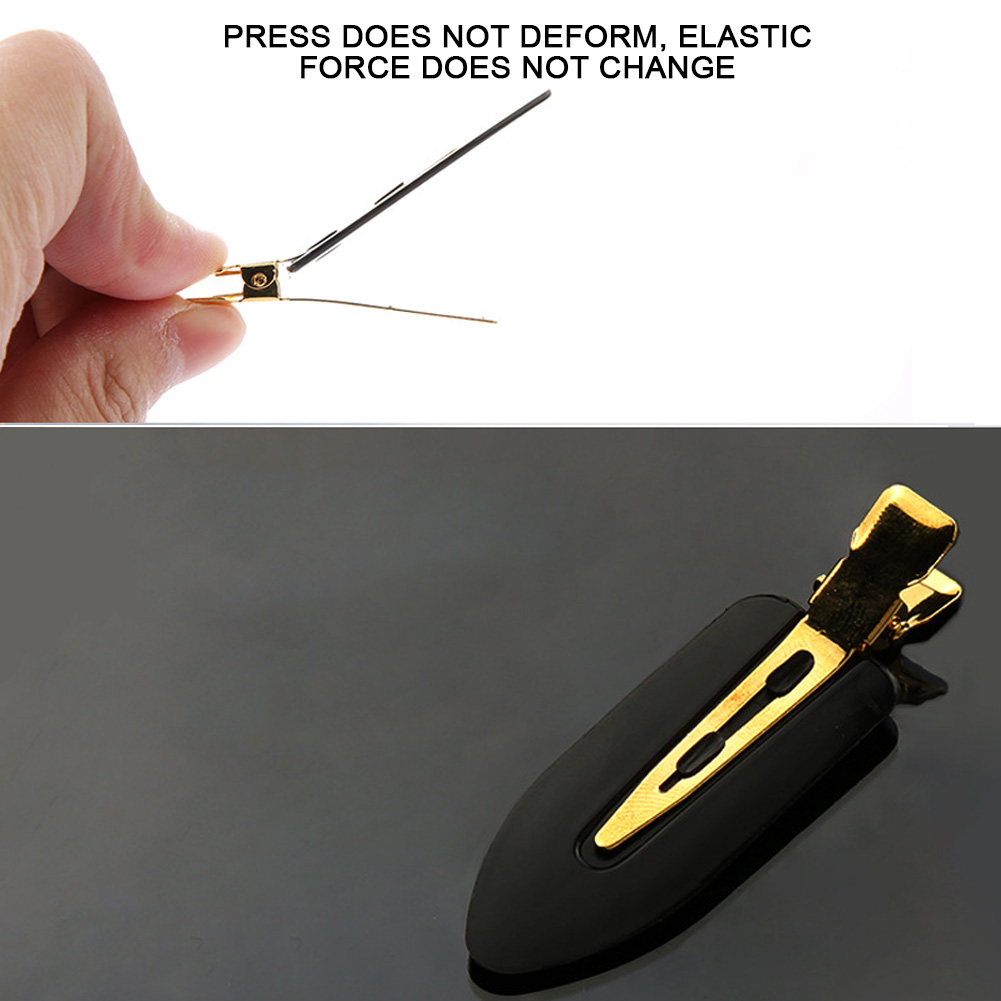 Eine Hand öffnet eine schwarze Haarspange mit Goldmetall. Die Spange ist wie ein abgeflachter Tropfen geformt. Schwarzer Hintergrund.