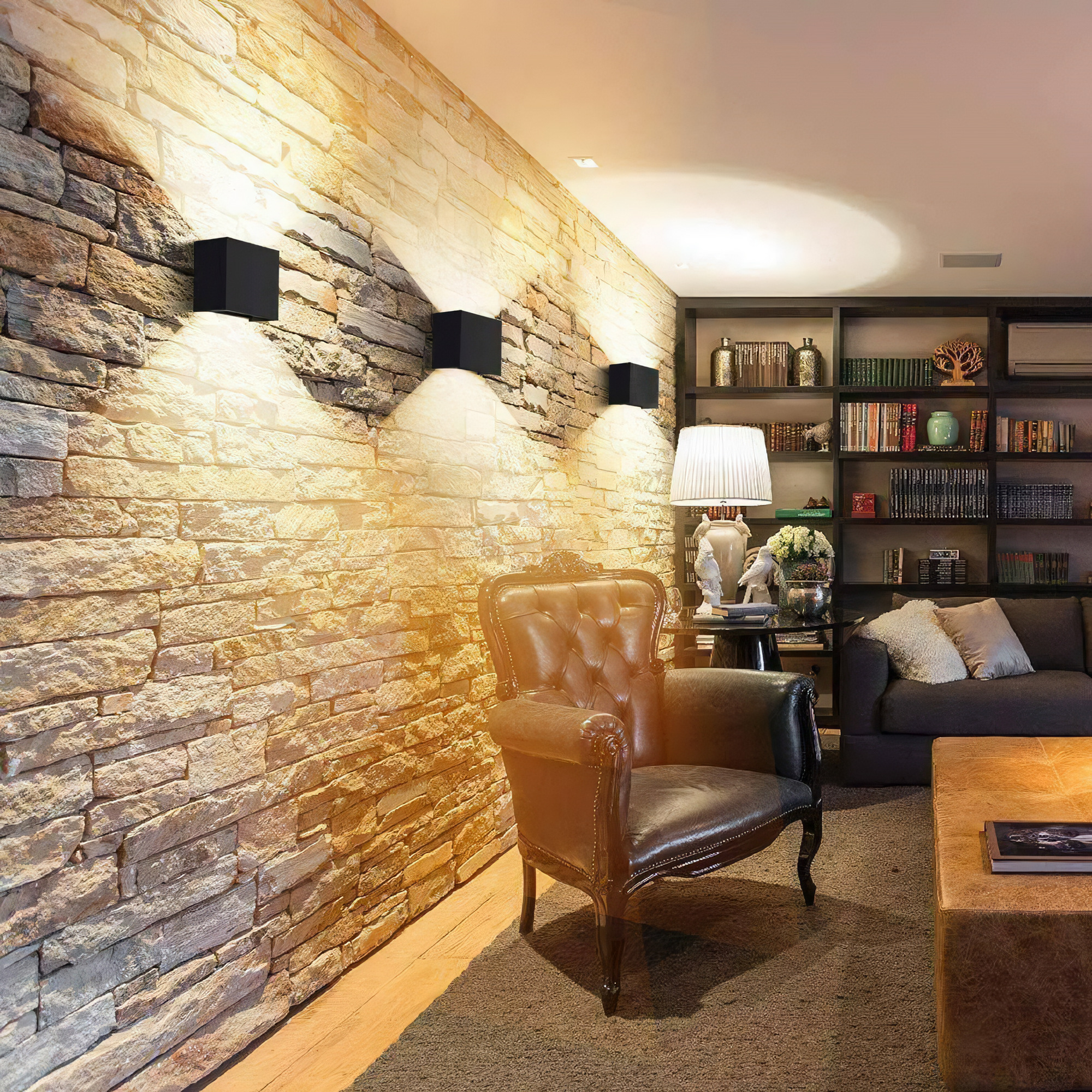 Ein Wohnzimmer mit einer Steinmauer. Drei schwarze quadratische Leuchten sind montiert. Ein Ledersessel, Sofa und Tisch sind vorhanden.