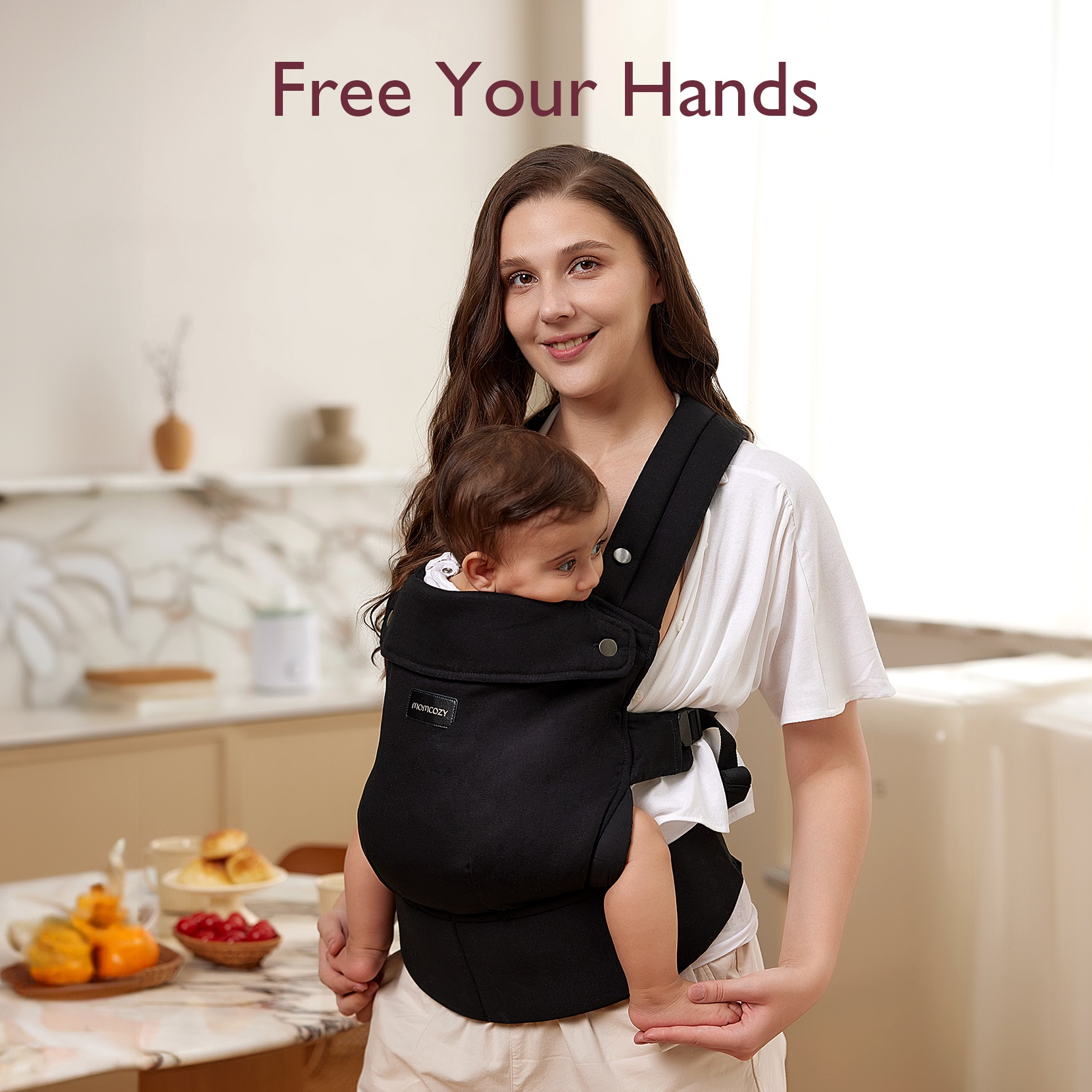 A woman and baby are in a black baby carrier. The woman smiles, and the scene is well-lit.