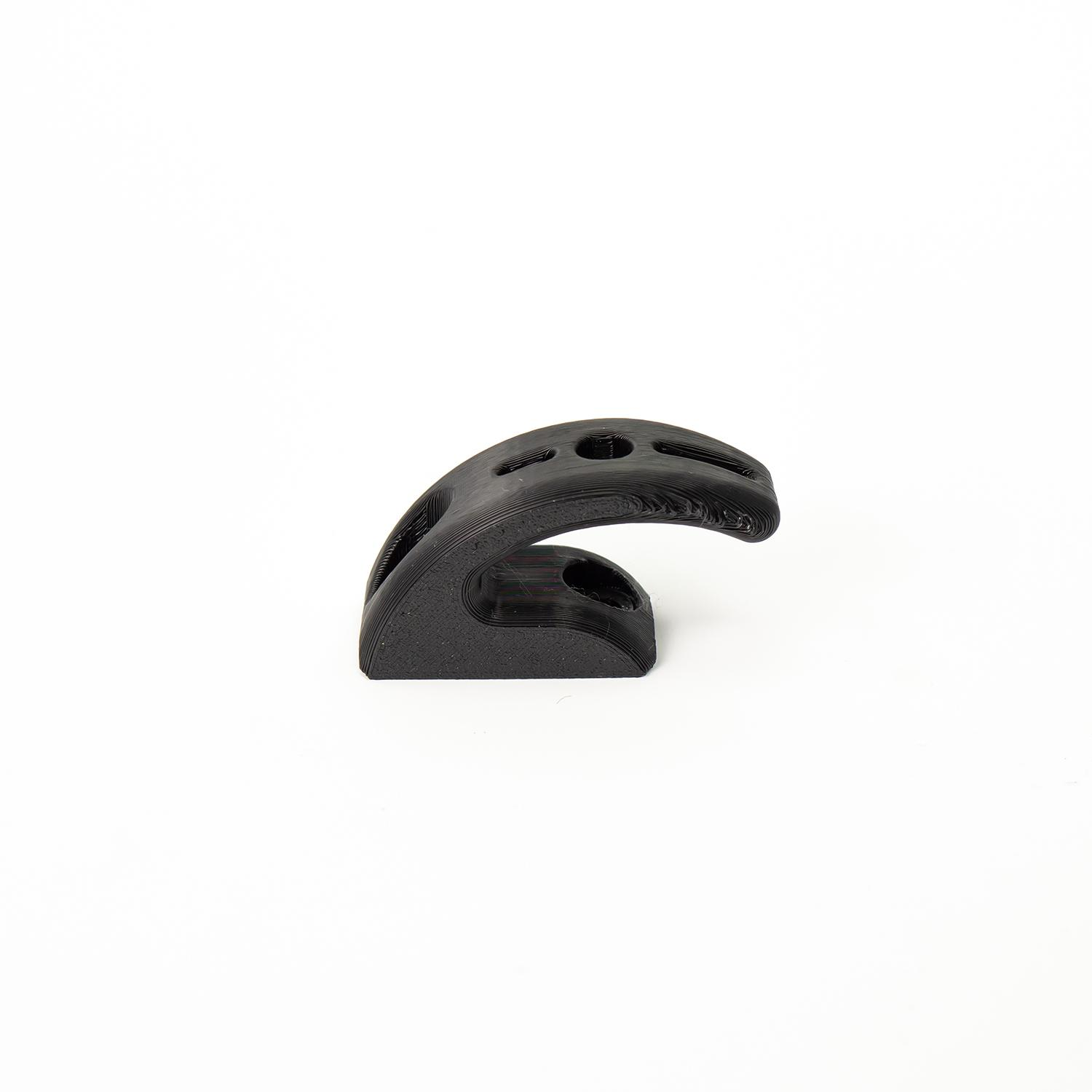 Un objeto de plástico negro, curvado, con dos agujeros y una base plana, sobre fondo blanco.