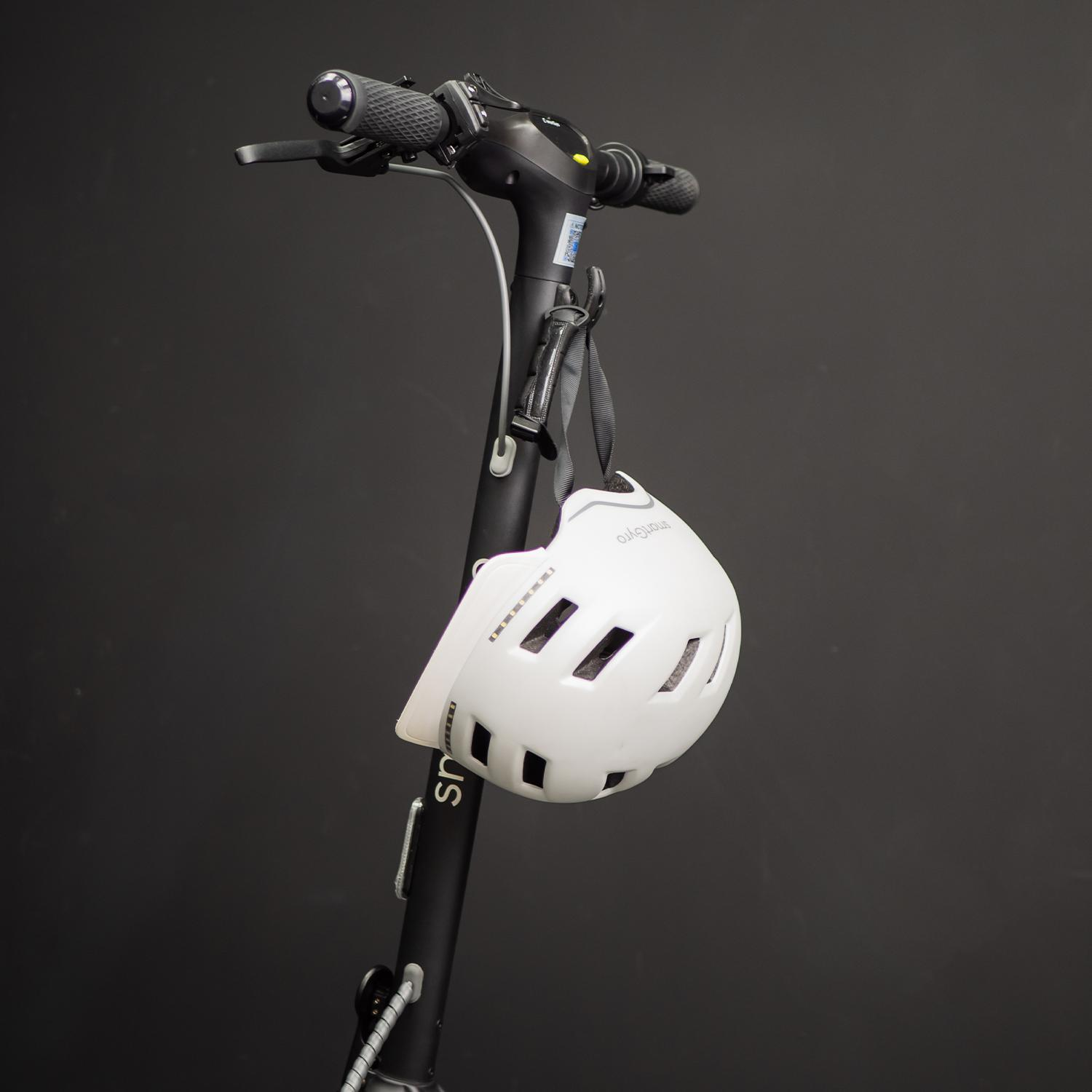 Un casco blanco cuelga del manillar de un patinete eléctrico. El fondo es oscuro.