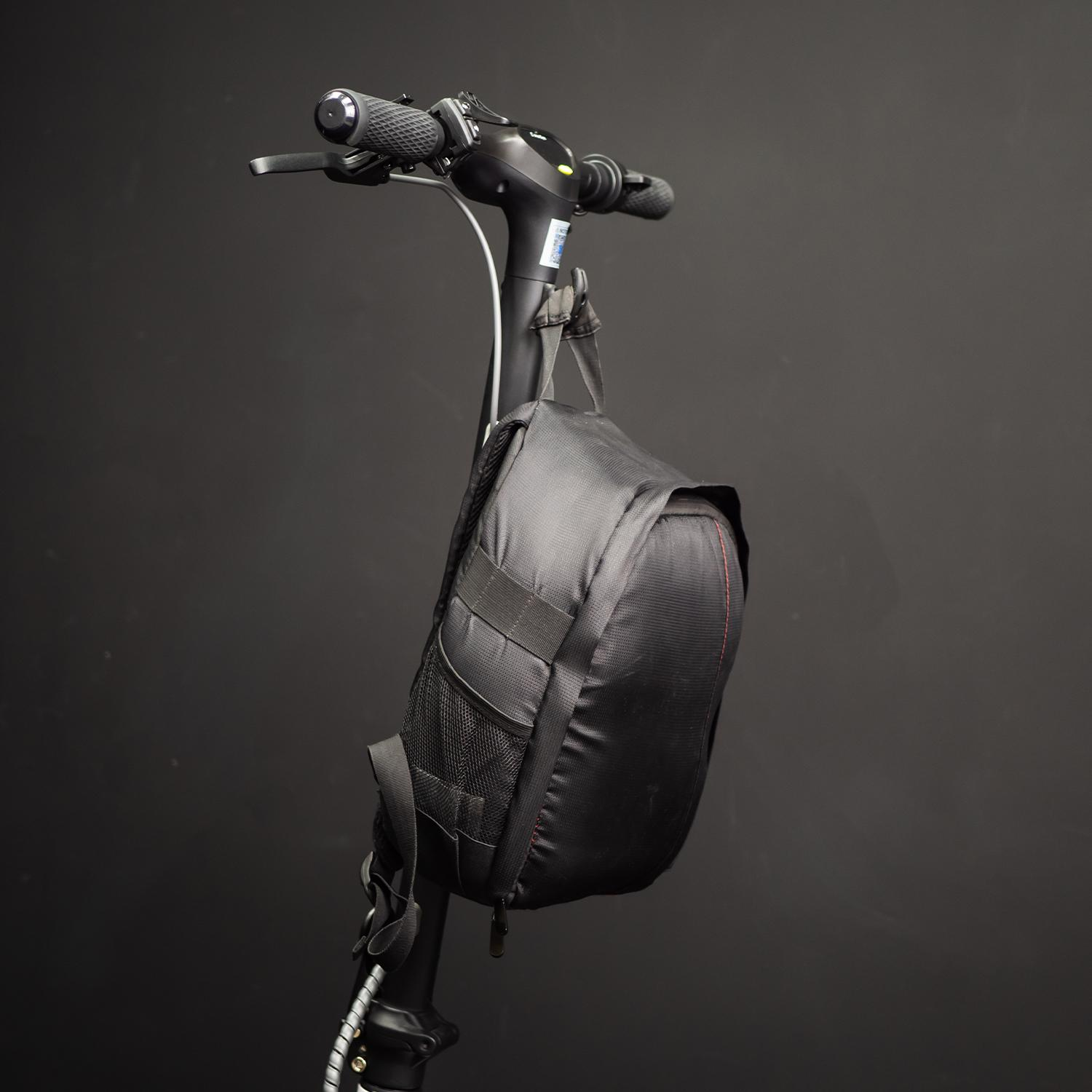 Una bolsa negra cuelga del manillar de un patinete eléctrico. El fondo es oscuro.