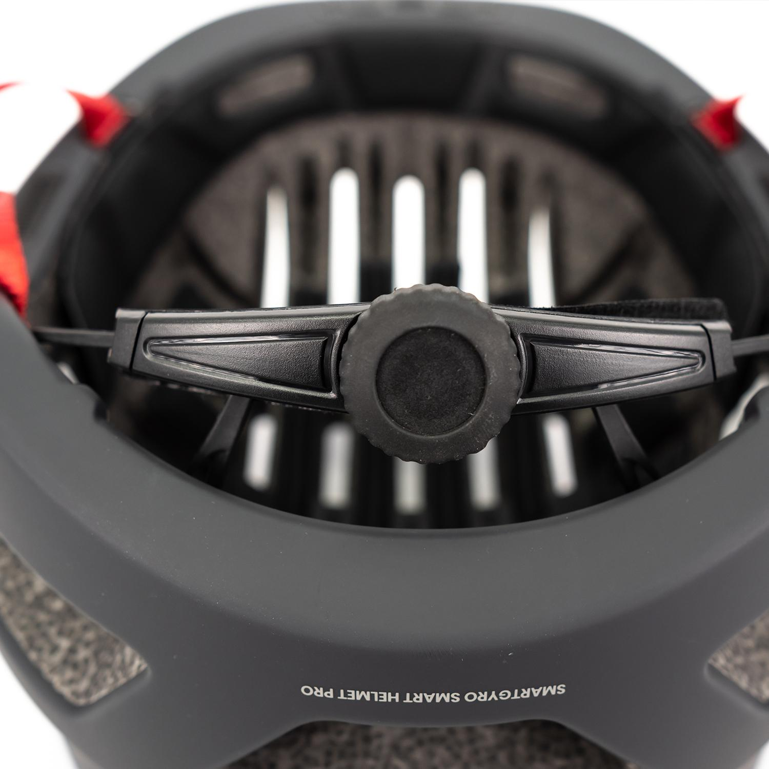 Vista interior de un casco negro, con rueda de ajuste, correas rojas y espuma interna.
