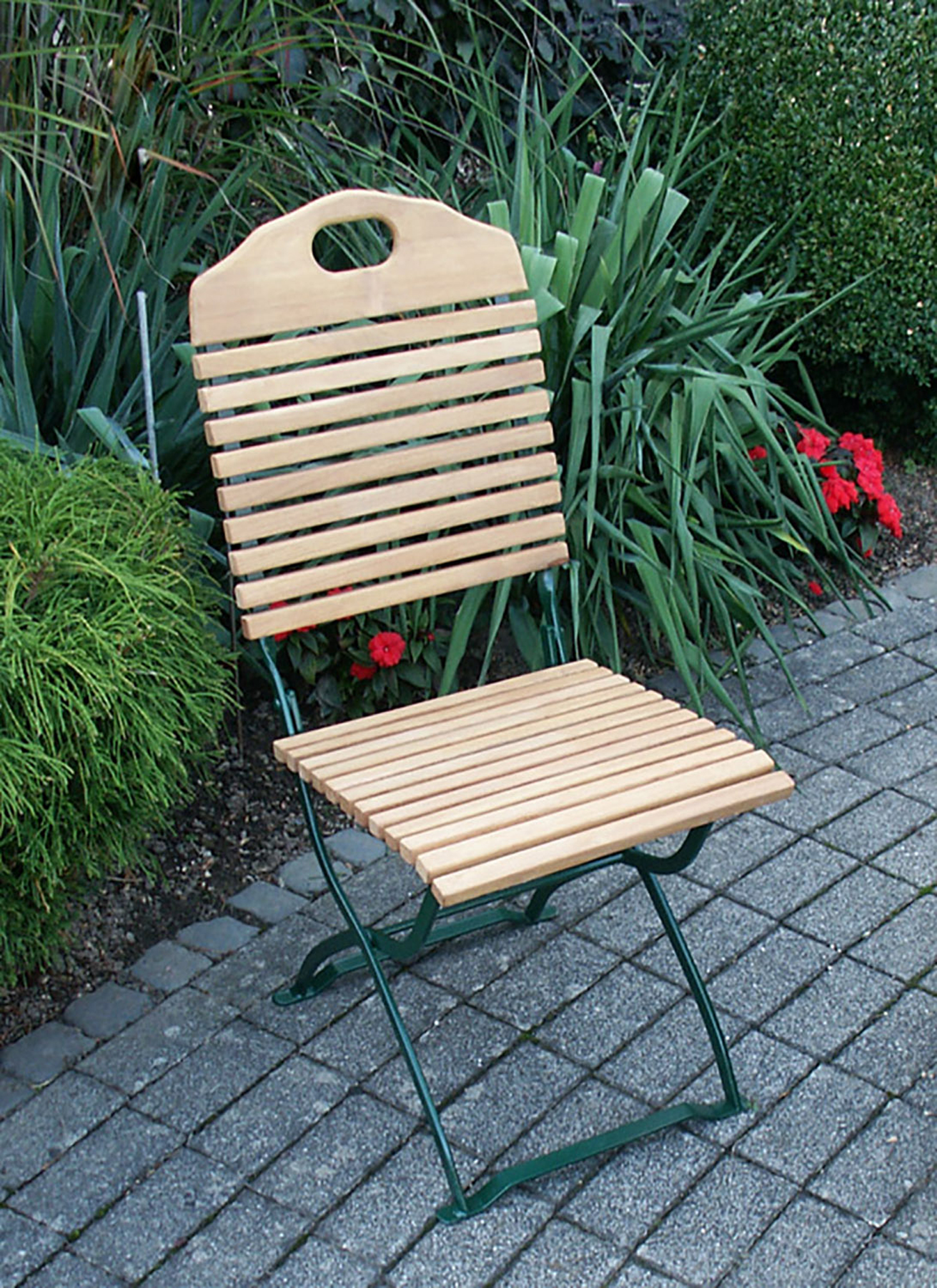 Holzklappstuhl mit grünem Rahmen auf einer Terrasse. Pflanzen im Hintergrund.