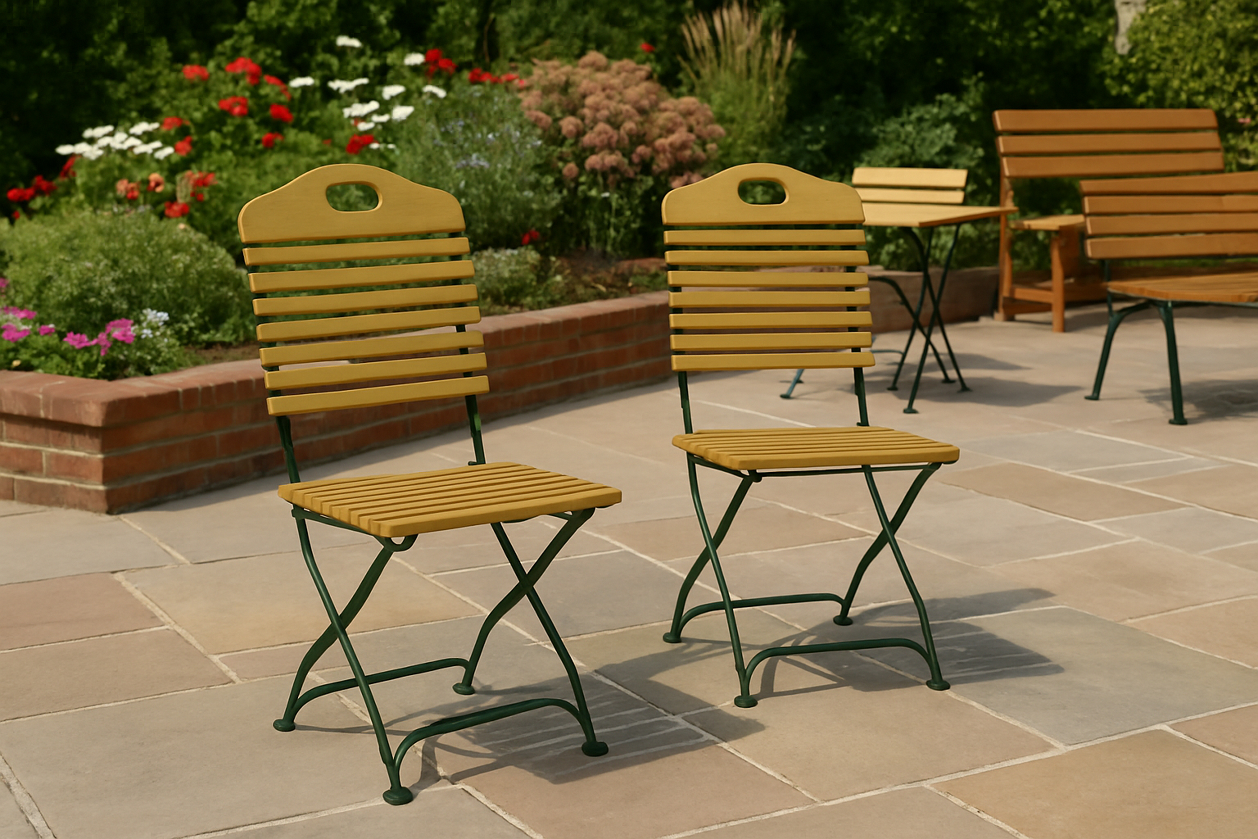 Zwei gelbe Holzstühle mit grünen Rahmen auf einer Terrasse, Garten und Pflanzen im Hintergrund.