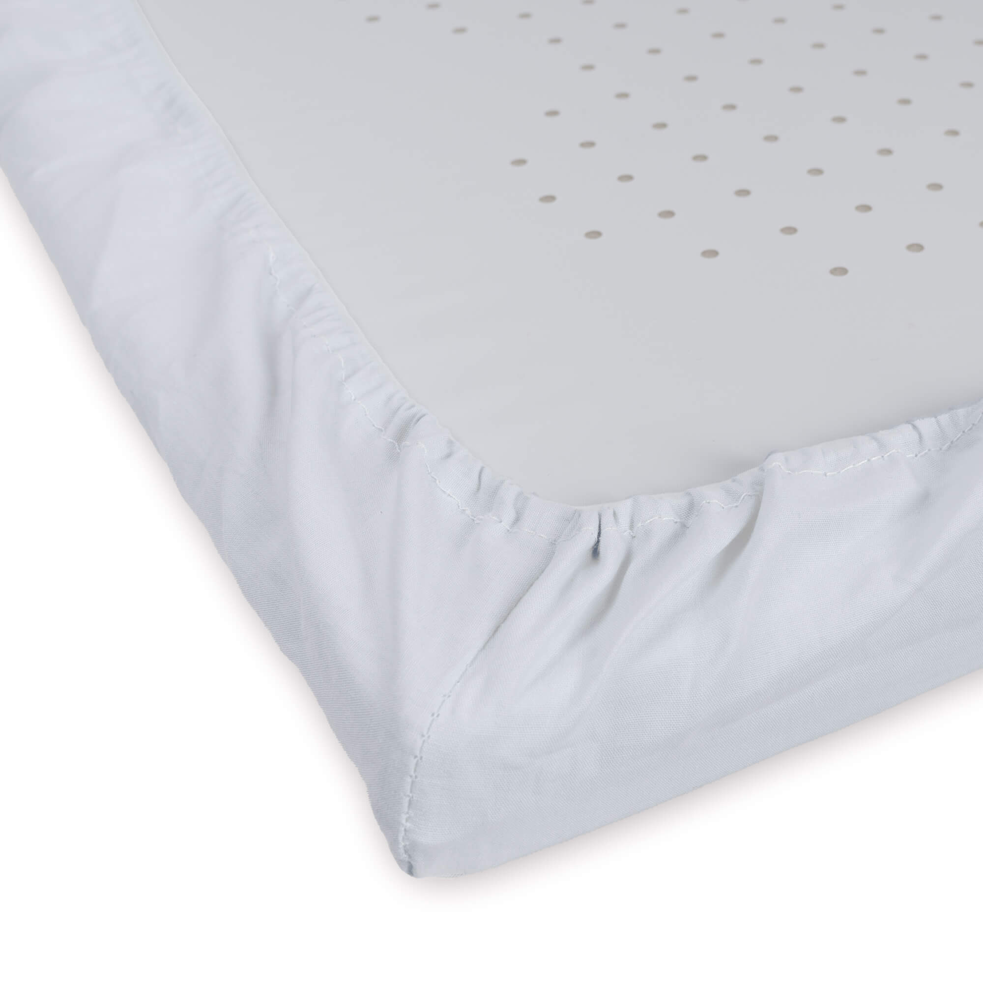 Primer plano de una sábana blanca para cuna. Se ve una esquina, con un patrón de puntos y borde elástico.