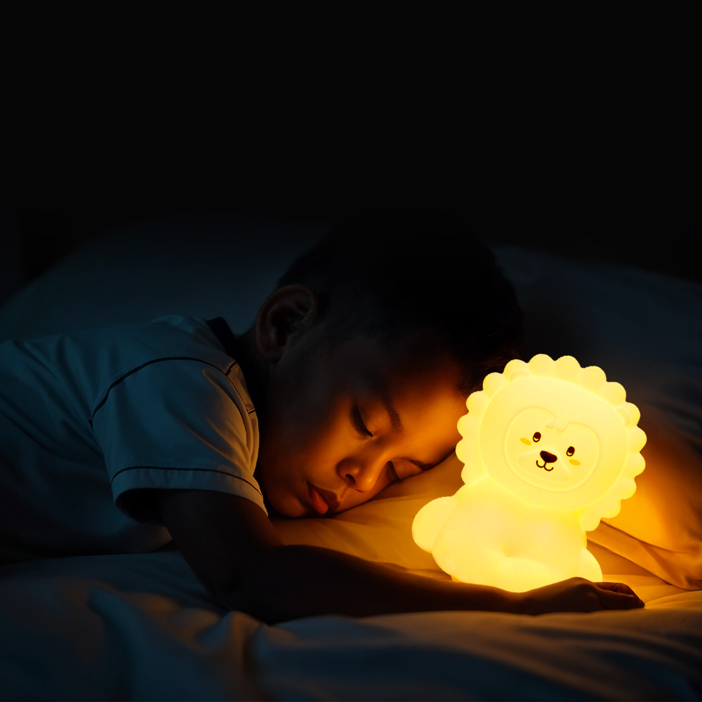 Un bambino che dorme accanto a una luce notturna a forma di leone su un letto, con sfondo scuro.