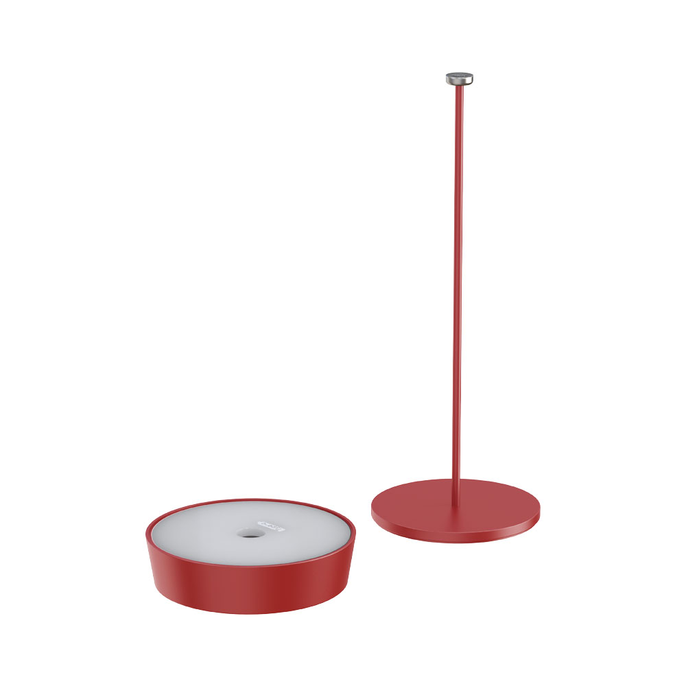 Una lampada rossa con base e stelo separati, isolata su bianco. La base è rotonda.
