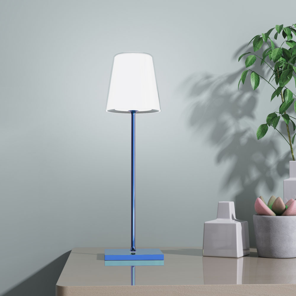 Lampada da tavolo con paralume bianco, stelo e base blu, su tavolo beige, accanto a piante.