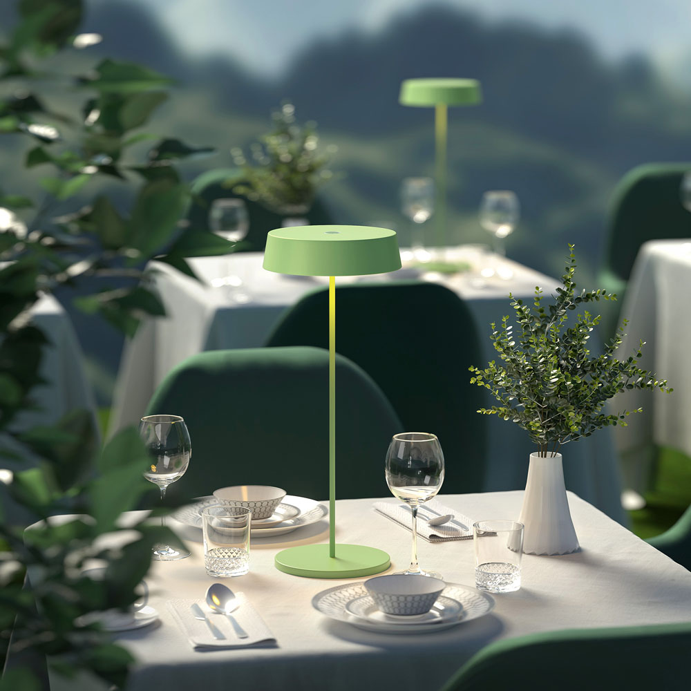 Un'apparecchiatura da tavolo da ristorante con lampada verde, bicchieri e piatti. Scena all'aperto.