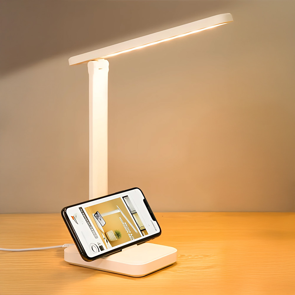 Una lampada da scrivania bianca con un telefono sulla sua base, posizionata su una superficie di legno.