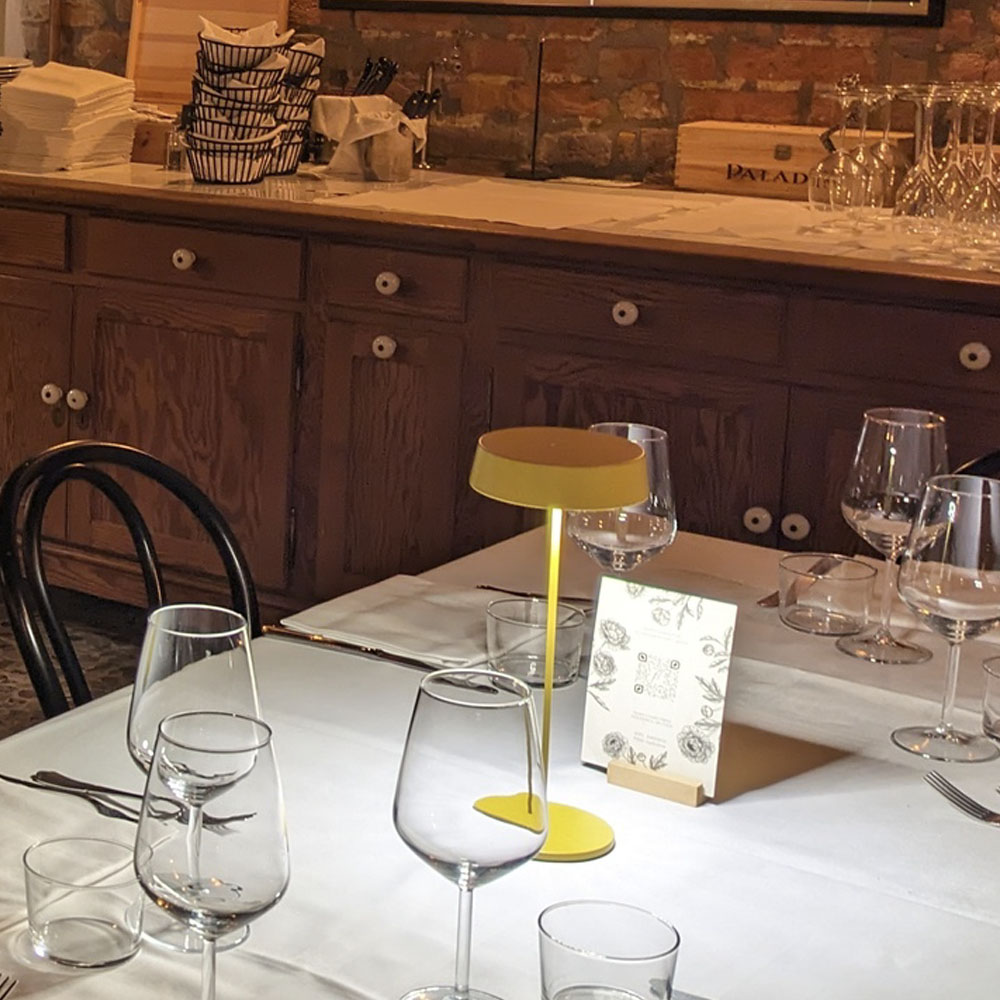 Un'apparecchiatura da tavolo di ristorante con una lampada gialla, bicchieri da vino e un menu.