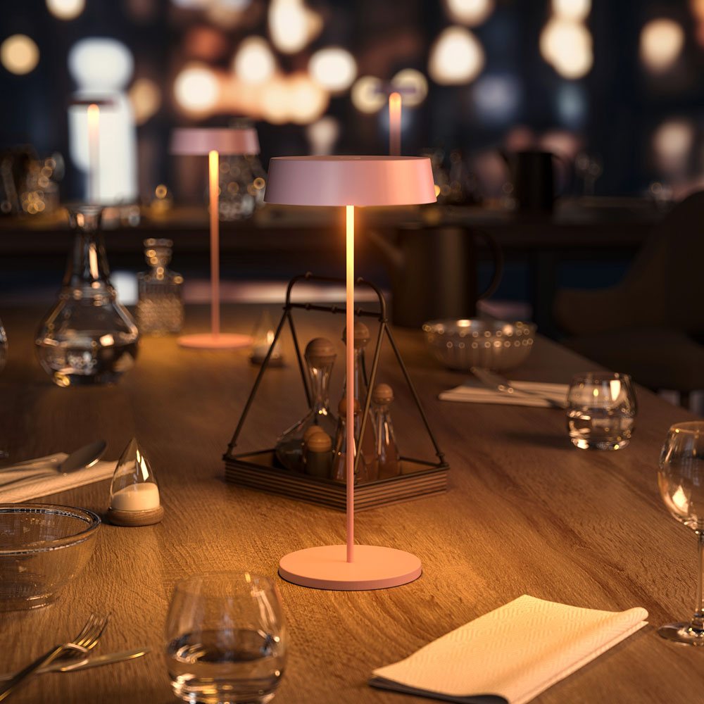 Una scena di ristorante scarsamente illuminata con lampade sui tavoli, bicchieri e decorazioni.