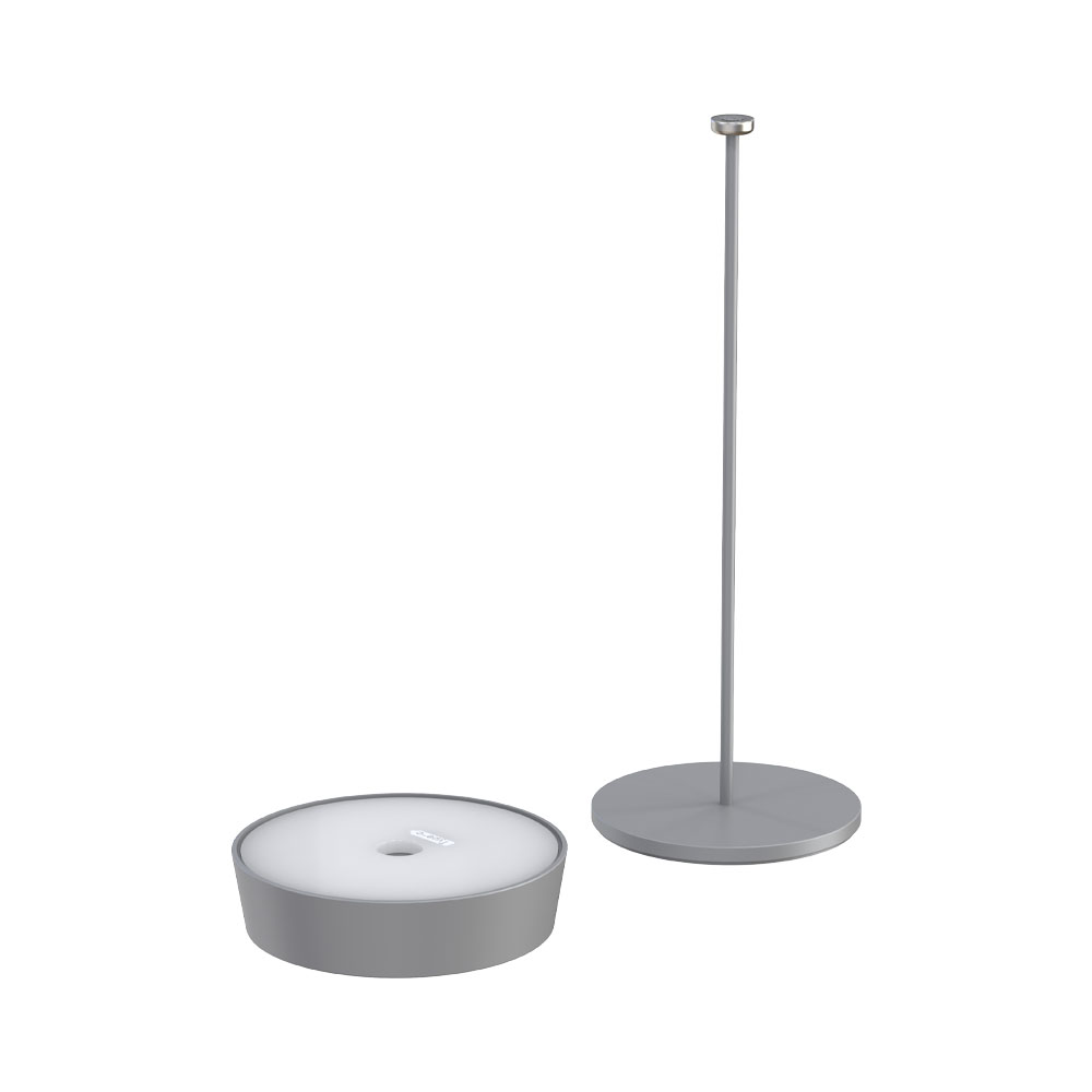 Una lampada grigia e una base staccata. La lampada ha una base circolare e un palo alto grigio.