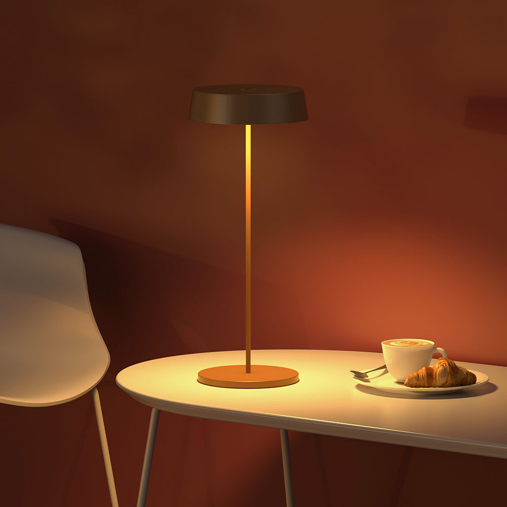 Una lampada su un tavolo accanto a una tazza di caffè e un croissant. Il muro è rosso.