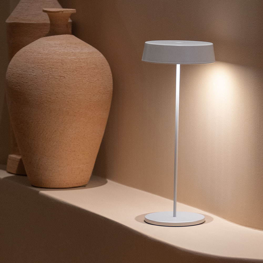 Una lampada bianca con base e paralume rotondi. Due grandi vasi di argilla sullo sfondo sfocato.