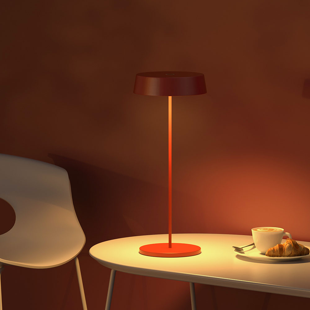 Una lampada rossa su un tavolo accanto a una tazza di caffè e un croissant. Il muro è rosso.