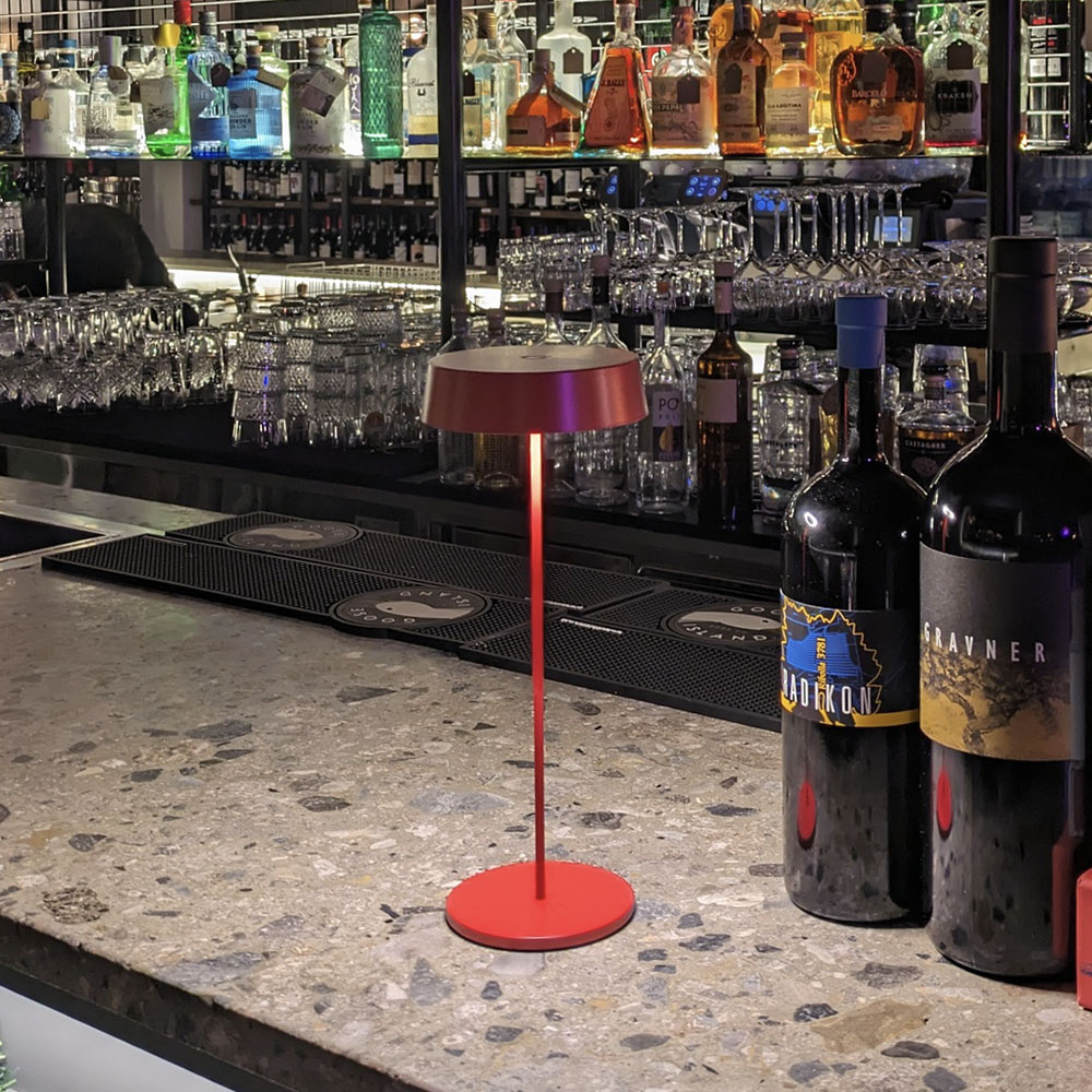 Una lampada rossa su un bancone di marmo. Ci sono bottiglie di alcolici sullo sfondo.