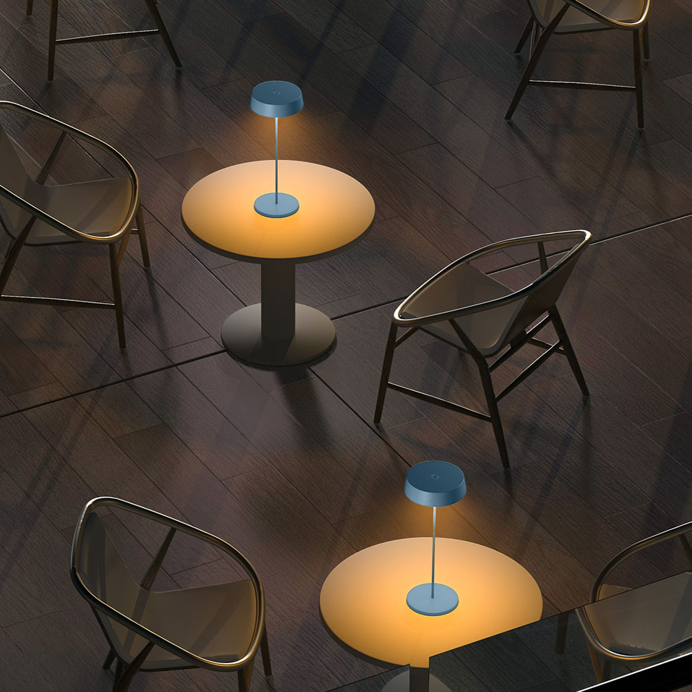 Diverse piccole lampade blu su tavoli rotondi in una stanza con sedie e pavimento in legno.