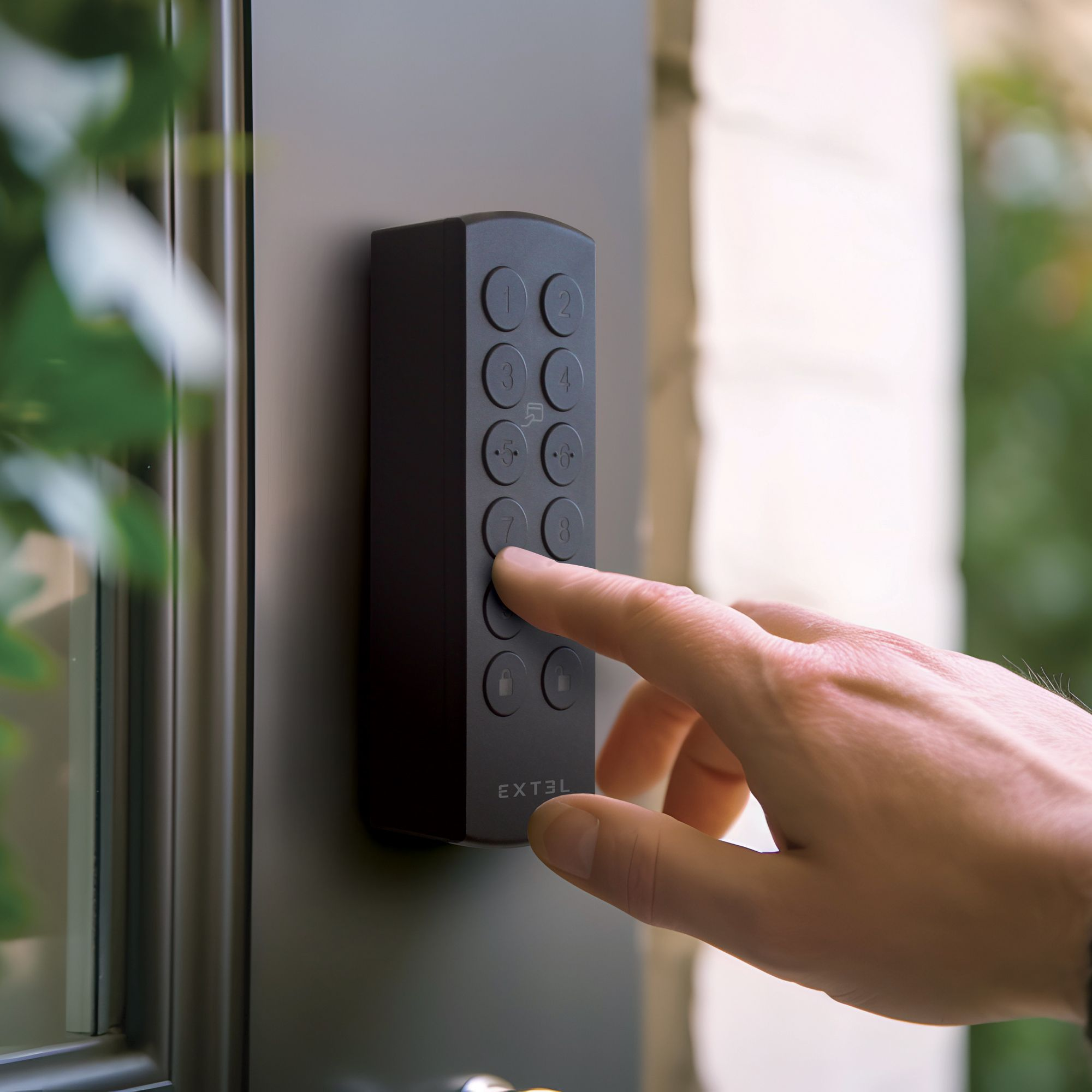 Una mano presionando un botón en una cerradura de puerta con teclado Extel negro, montada en una puerta oscura.