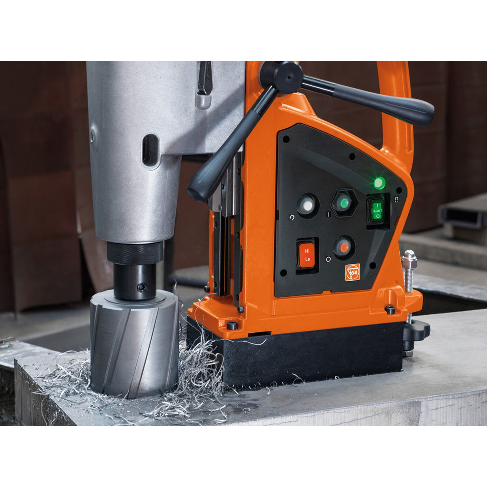 Eine orangefarbene Bohrmaschine auf Metall mit Metallspänen. Sie hat Knöpfe, einen Griff und Lichter. Der Hintergrund ist unscharf.