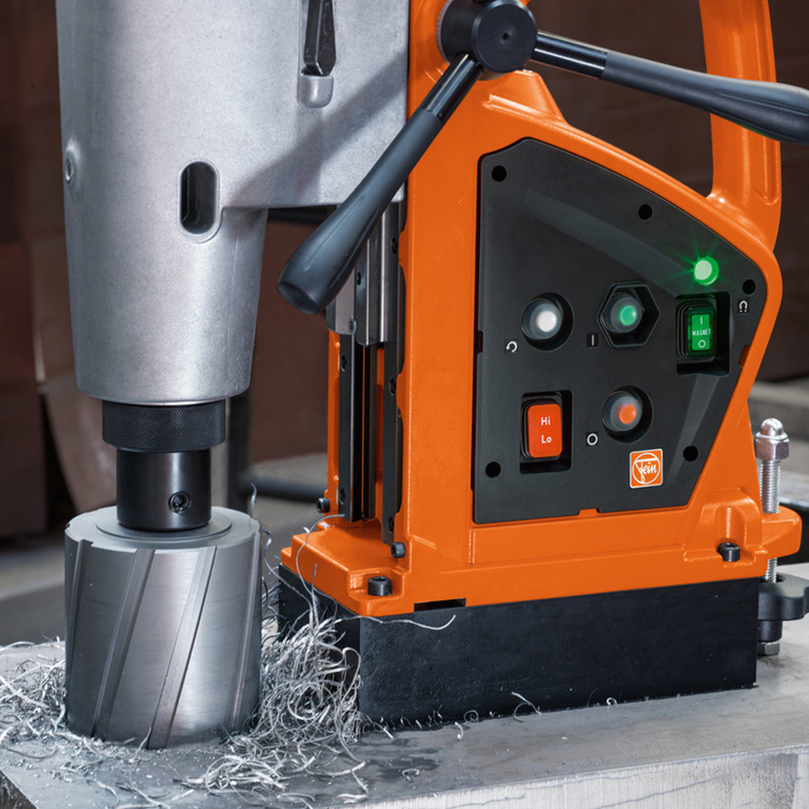 Eine orangefarbene Bohrmaschine auf Metall mit Metallspänen. Sie hat Knöpfe, einen Griff und Lichter. Der Hintergrund ist unscharf.
