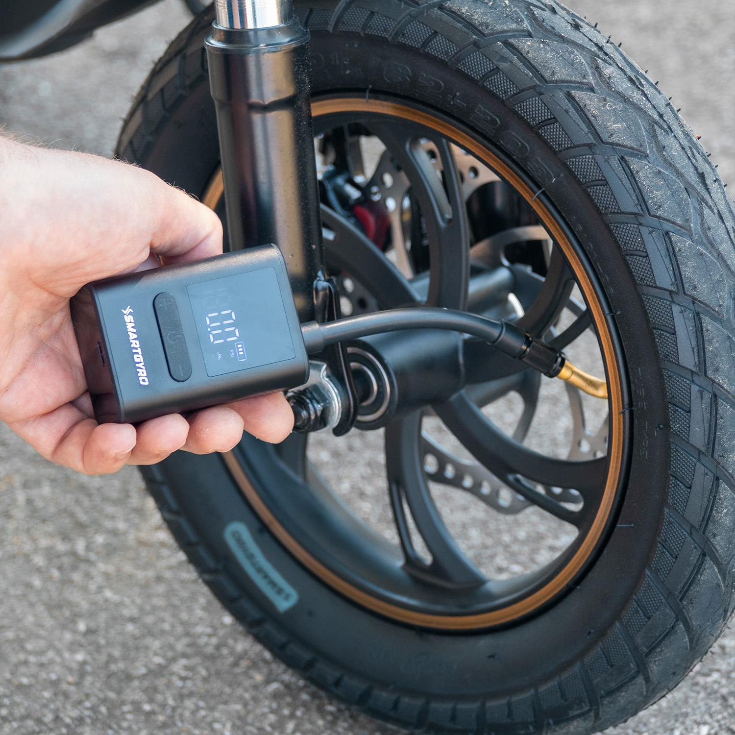Una persona inflando un neumático de un scooter con un inflador de neumáticos negro. El neumático es negro.
