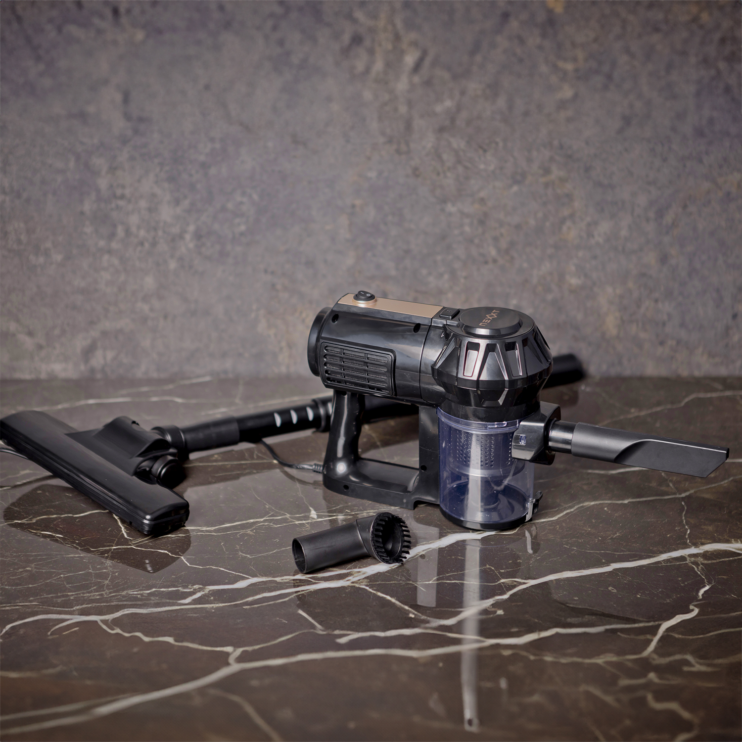 A black and gray cordless vacuum cleaner with attachments on a marble surface. Background is grey.